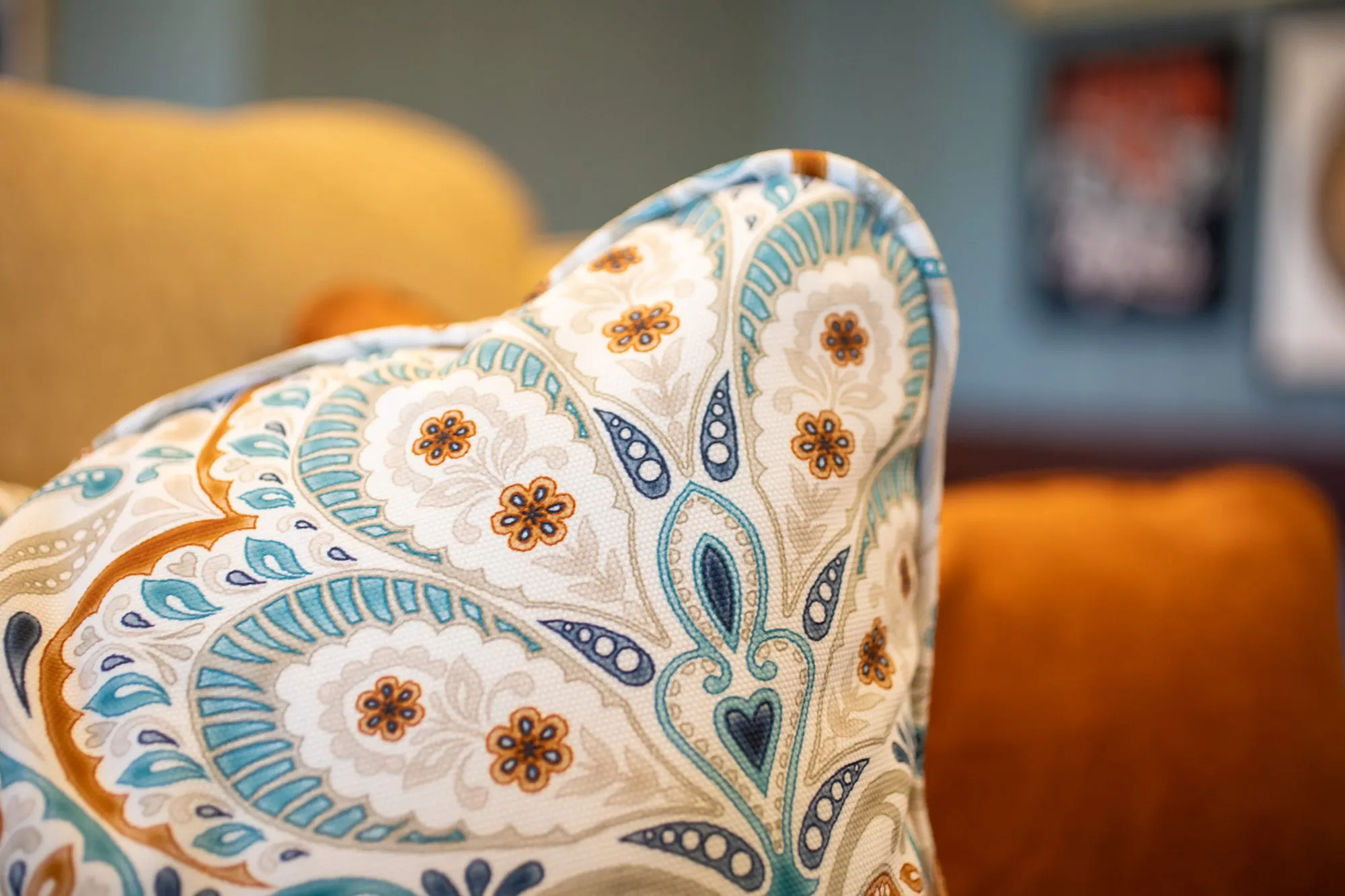 Senior living interior detail: paisley pillow in teal, orange and navy on a camel sofa