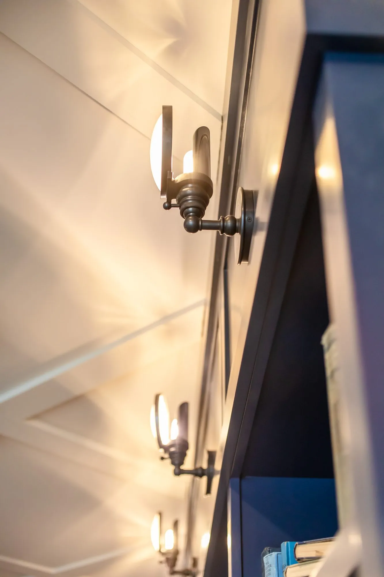 Senior living interior detail: black and brass wall sconces lighting white shiplap beside navy shelving