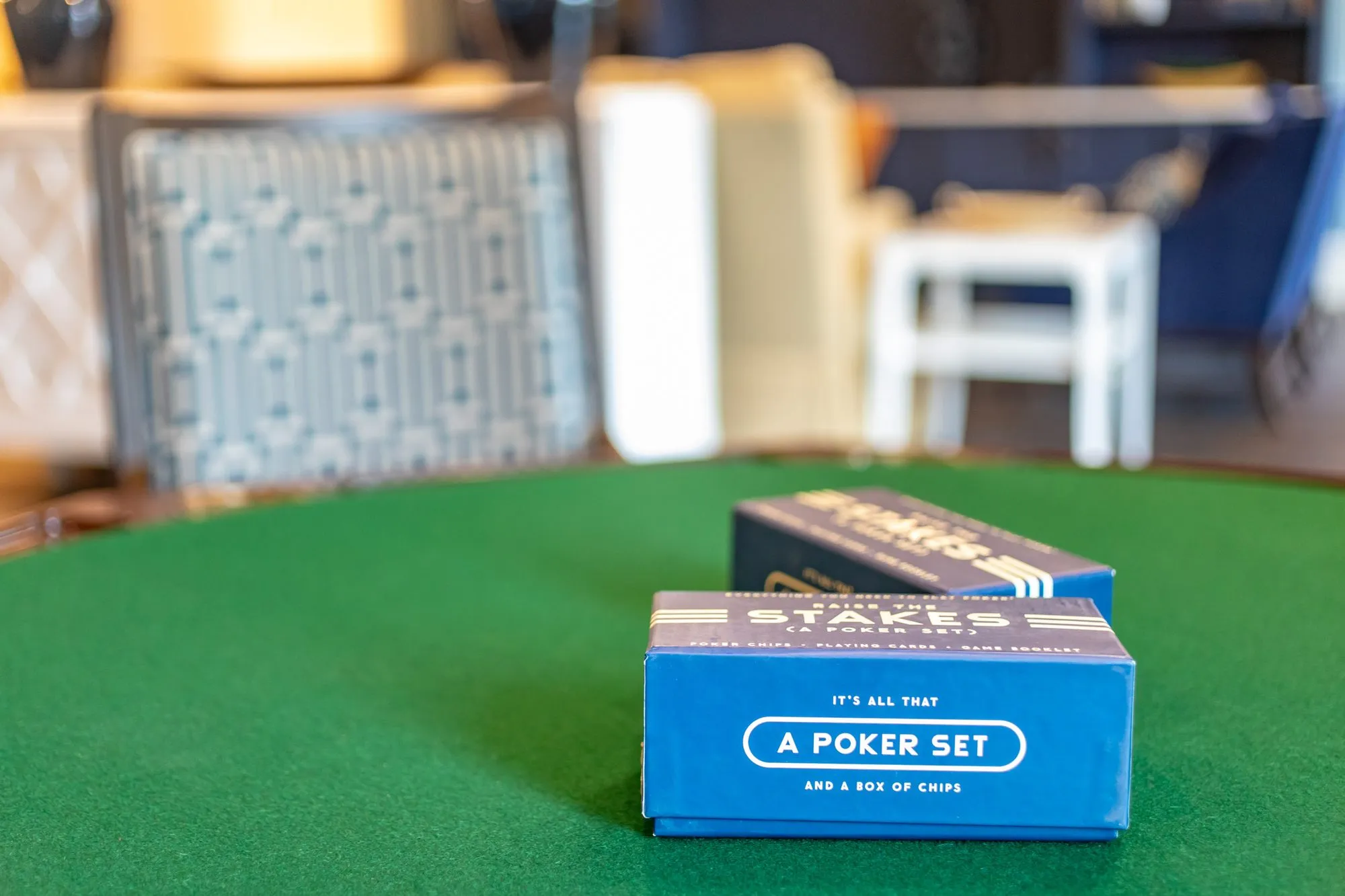 Senior living interior detail: two boxed poker sets on a green felt card table, chairs blurred behind