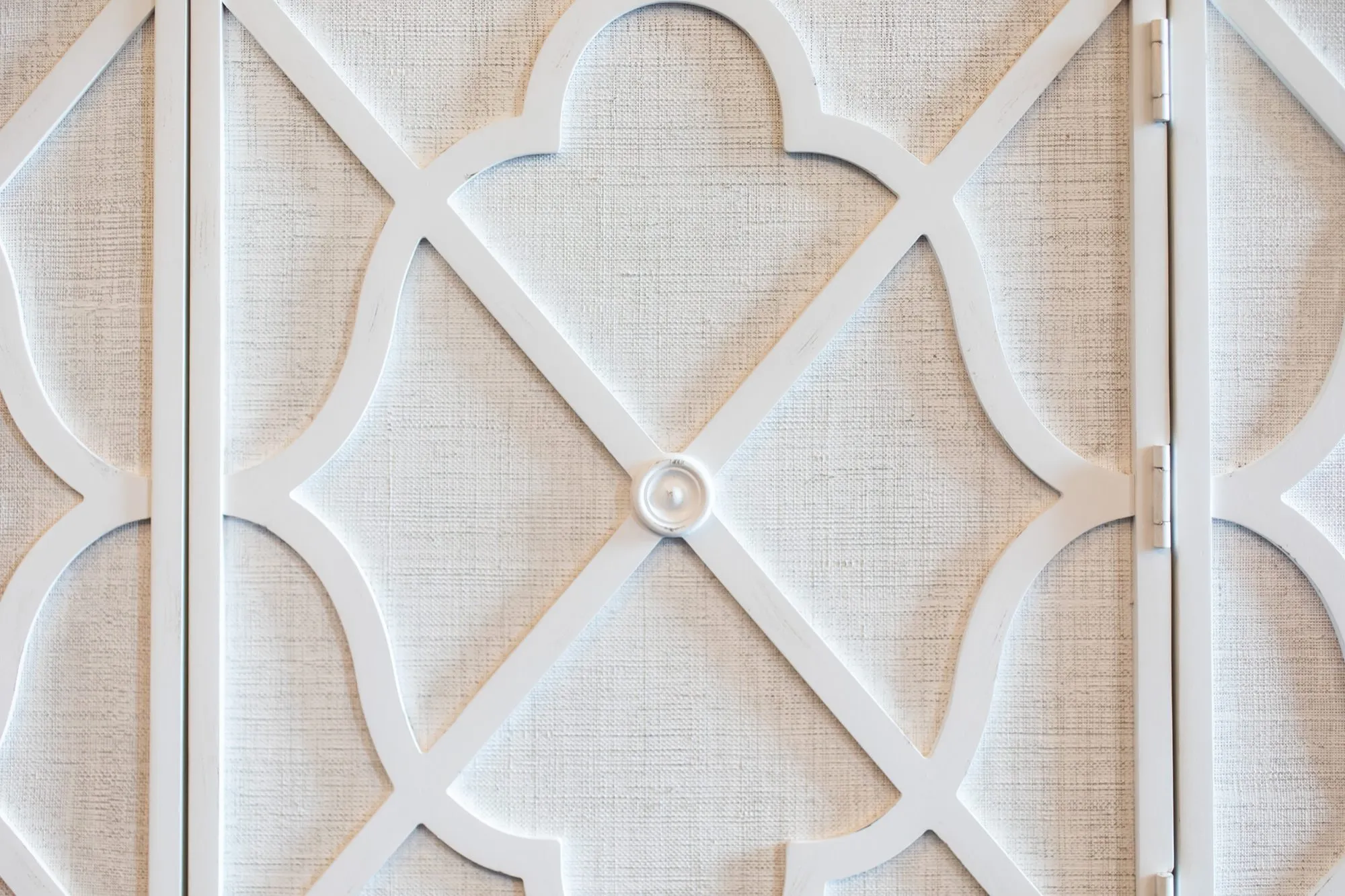 Senior living interior detail: white quatrefoil fretwork over linen panels on cabinet doors