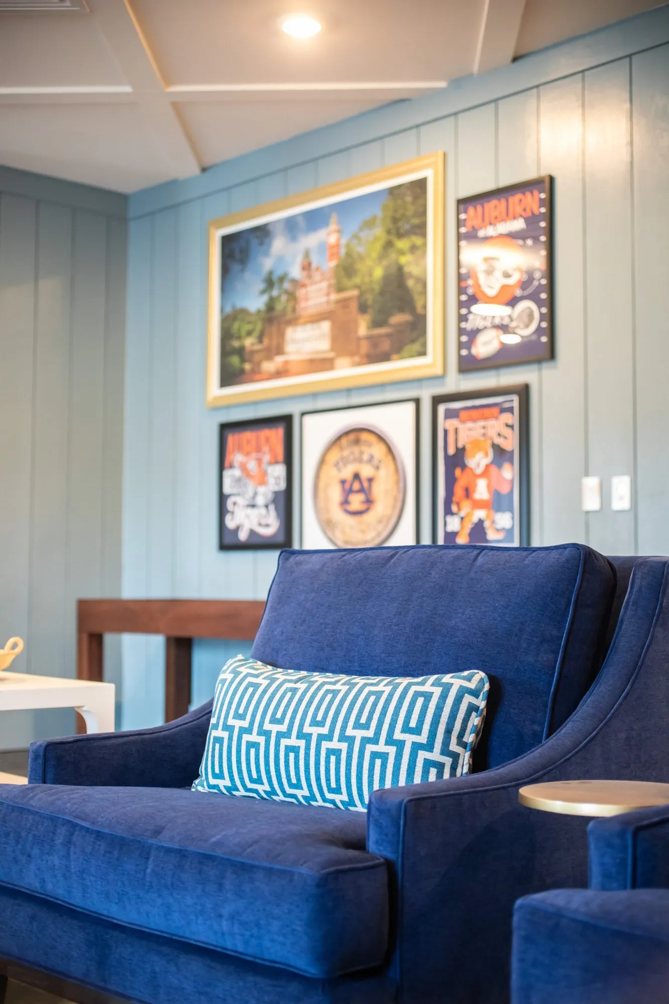 Senior living interior detail: navy velvet armchair below framed college sports posters on pale blue shiplap
