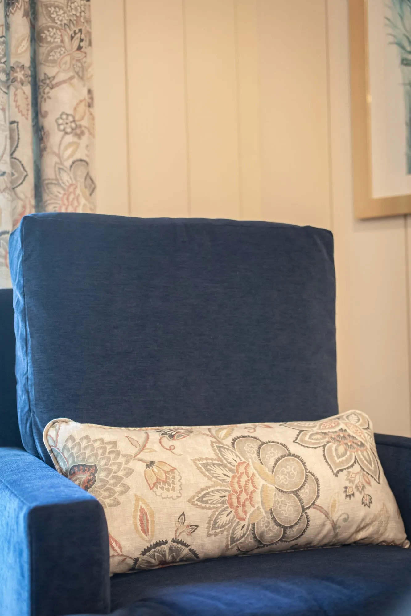 Senior living interior detail: navy armchair with a floral lumbar pillow beside floral drapery