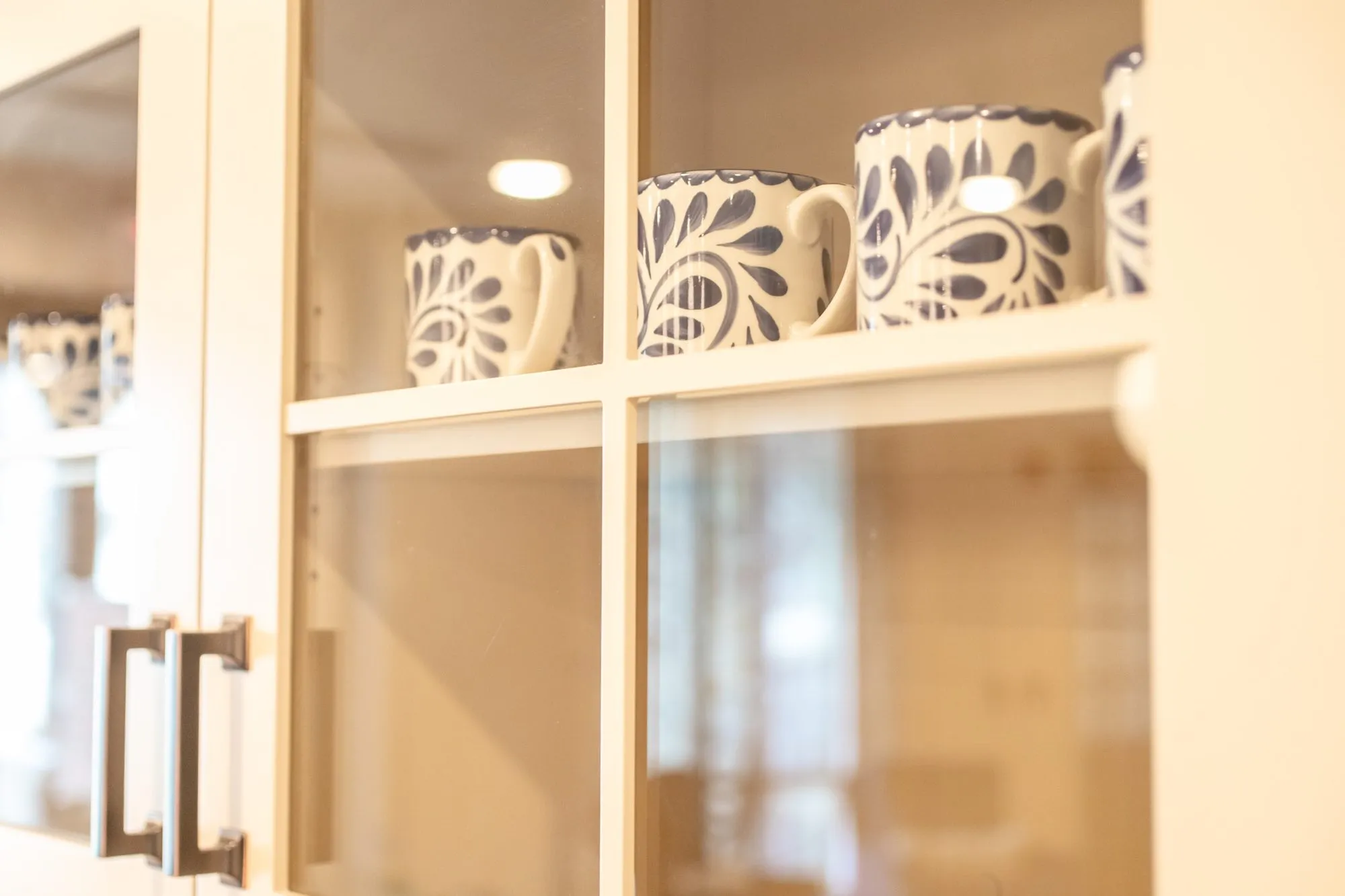 Senior living interior detail: blue and white floral mugs on a glass front cabinet shelf