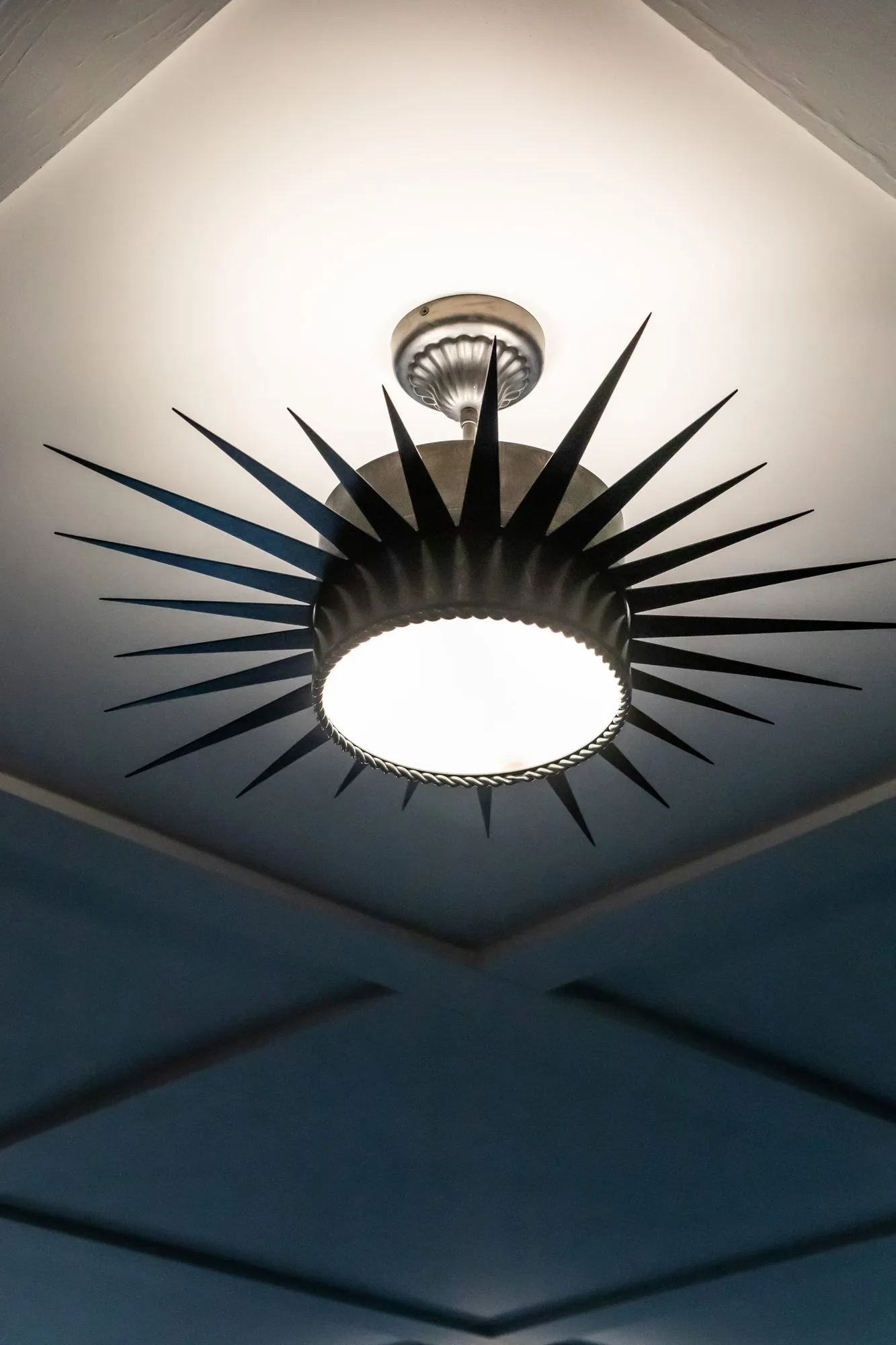 Senior living interior detail: black starburst ceiling light seen from below against a navy coffered ceiling