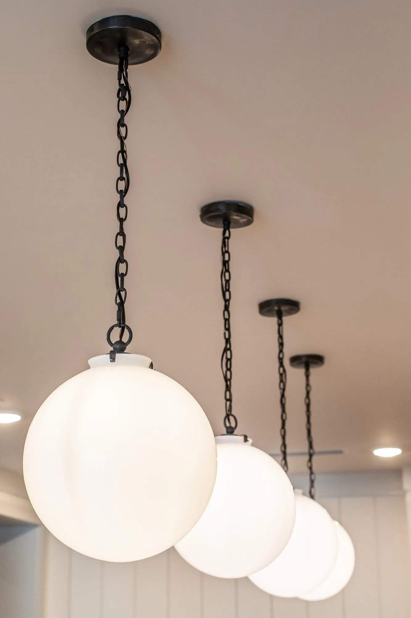 Senior living interior detail: row of white opal globe pendants on black chains receding along a ceiling