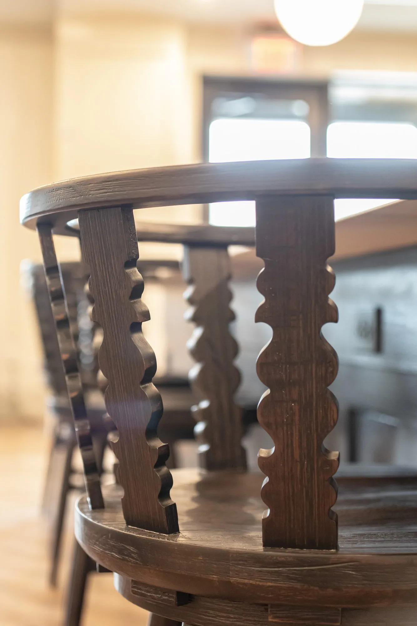 Senior living interior detail: dark wood chair back with carved spindles, a dining room blurred behind