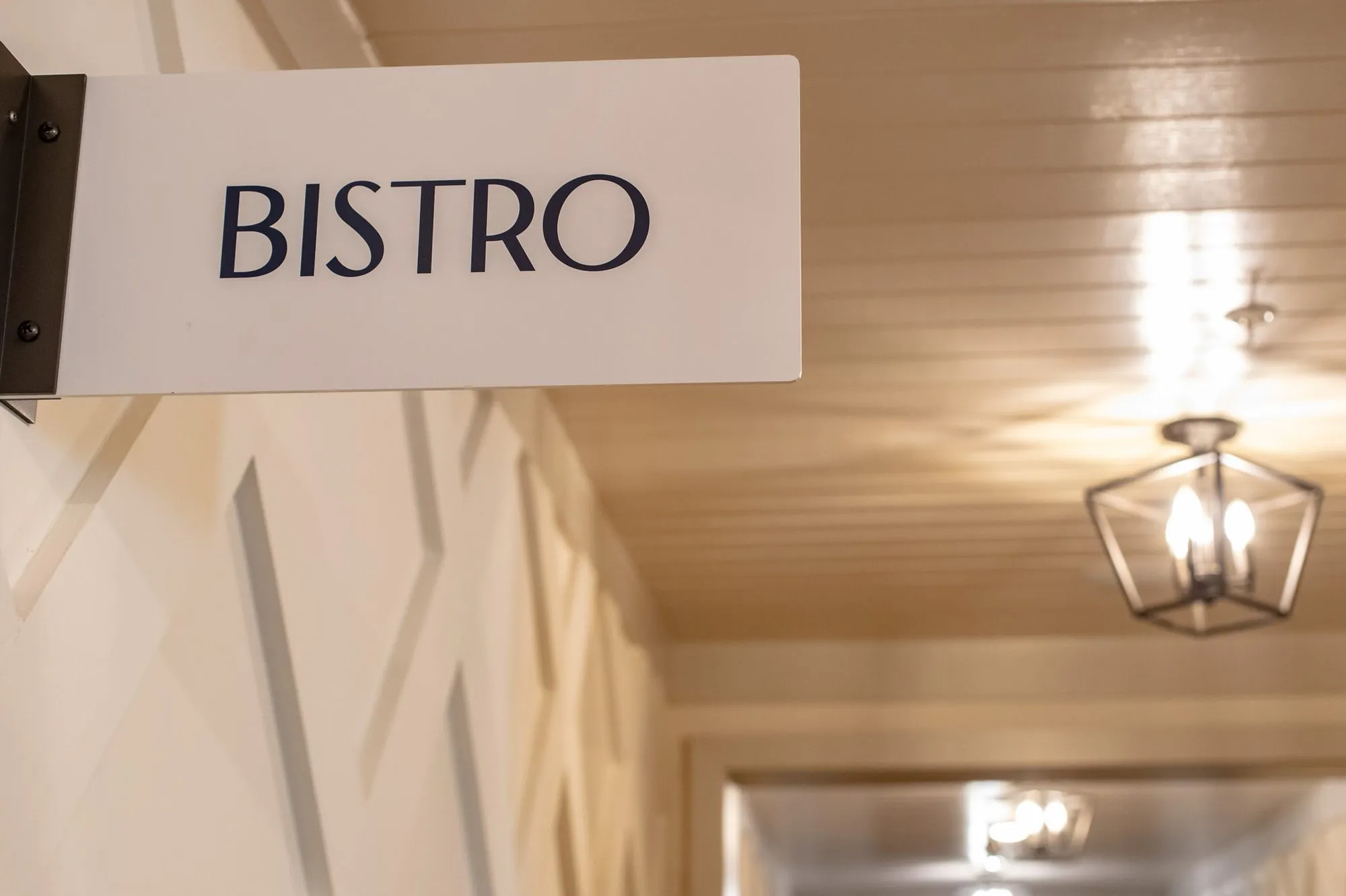 Senior living corridor with a Bistro sign projecting from white lattice panelling, a lantern pendant beyond