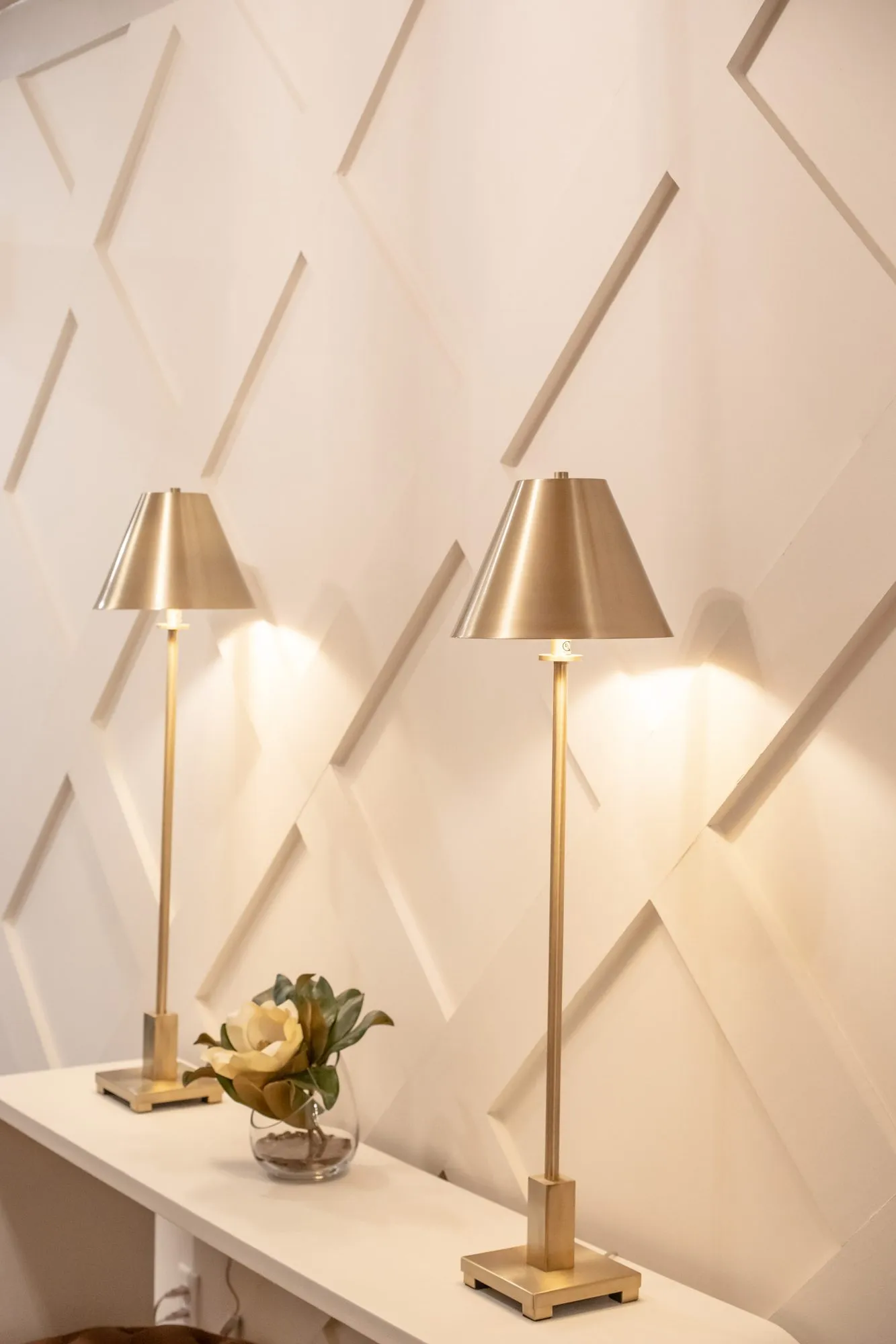 Senior living interior detail: two brass candlestick lamps on a white console against diamond panelled millwork
