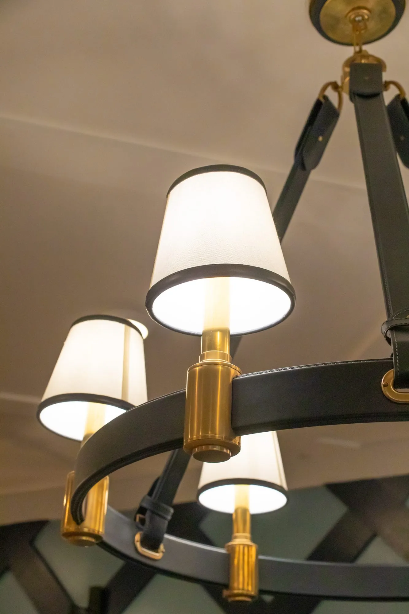 Senior living interior detail: looking up at a black and brass chandelier with white shades