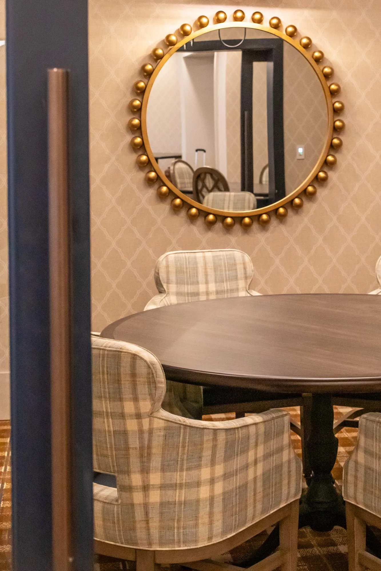 Senior living private dining room past a doorframe, plaid chairs at a round table below a gilt beaded mirror