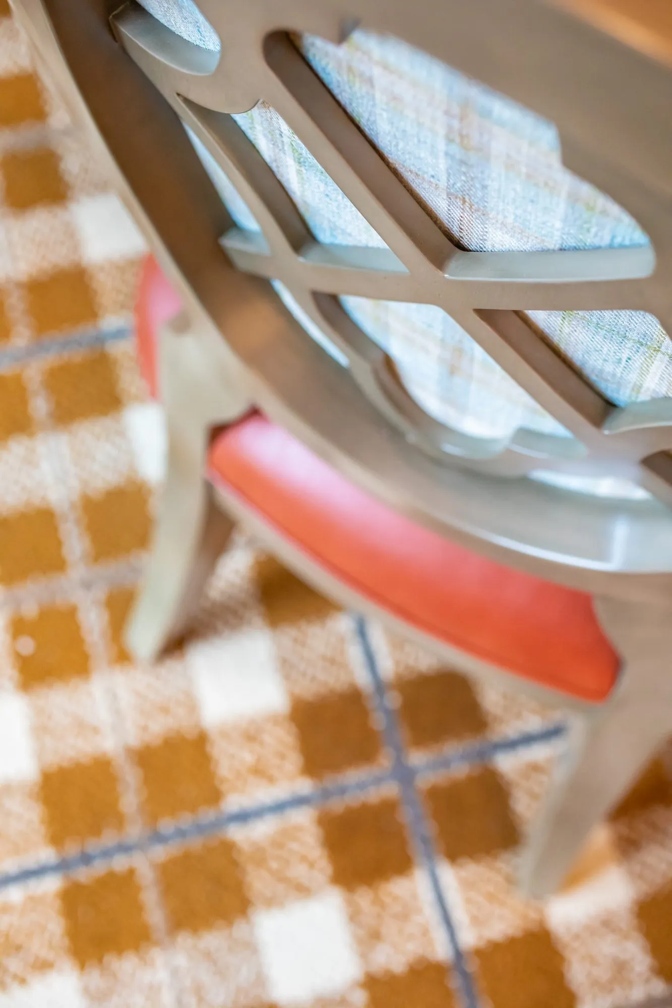 Senior living interior detail: quatrefoil back chair with a coral seat on orange plaid carpet