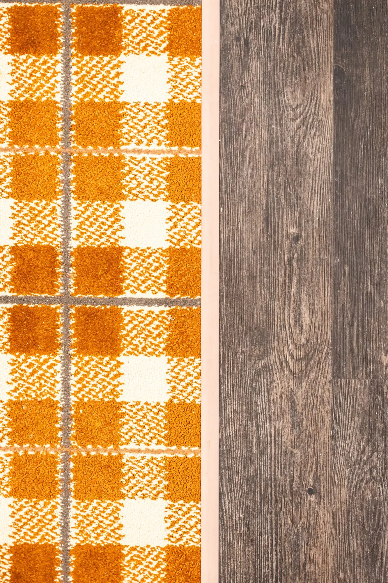 Senior living interior detail: orange and cream plaid carpet meeting dark wood plank flooring