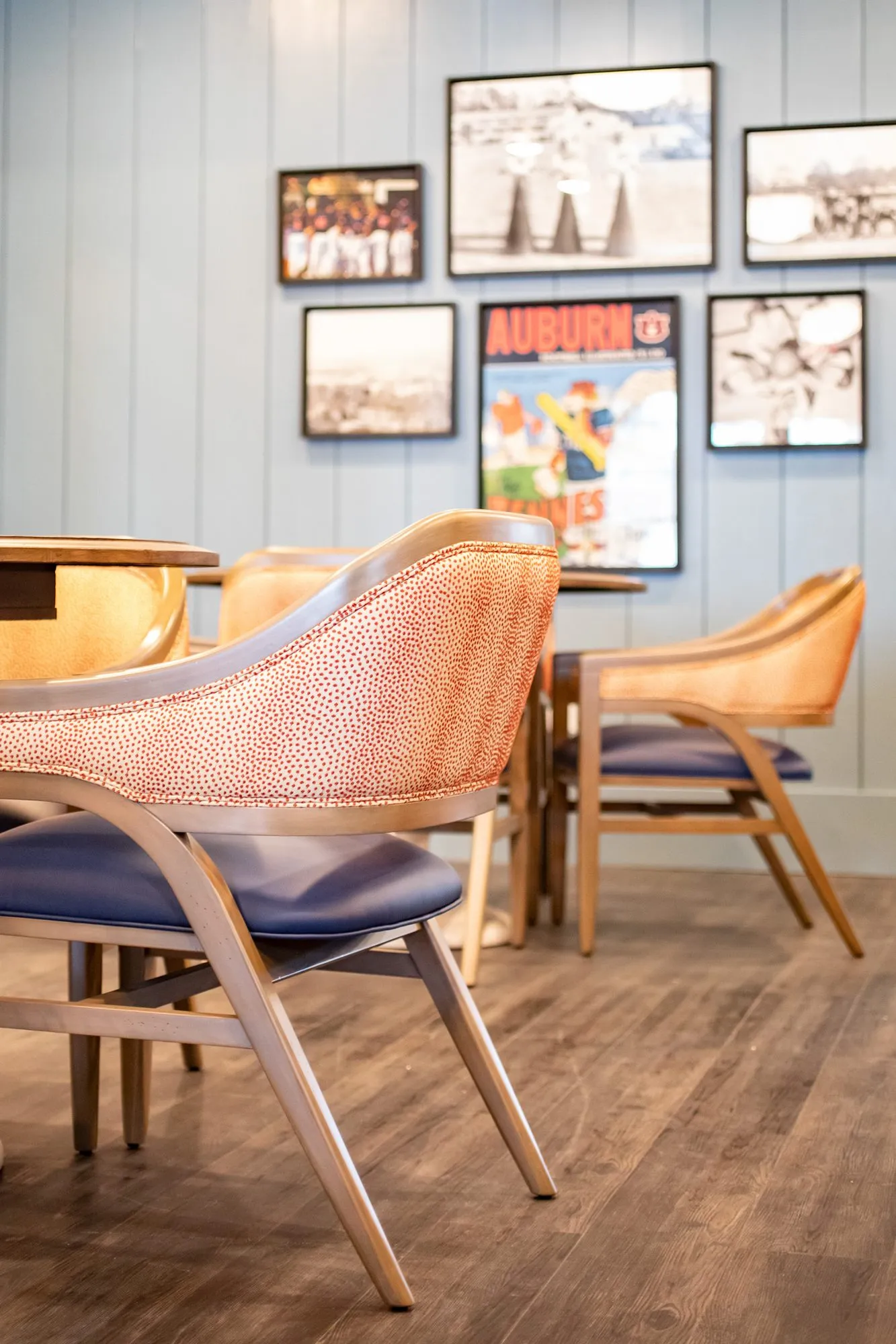 Senior living pub with coral dot chairs at small tables below vintage sports photos and an Auburn poster on blue shiplap