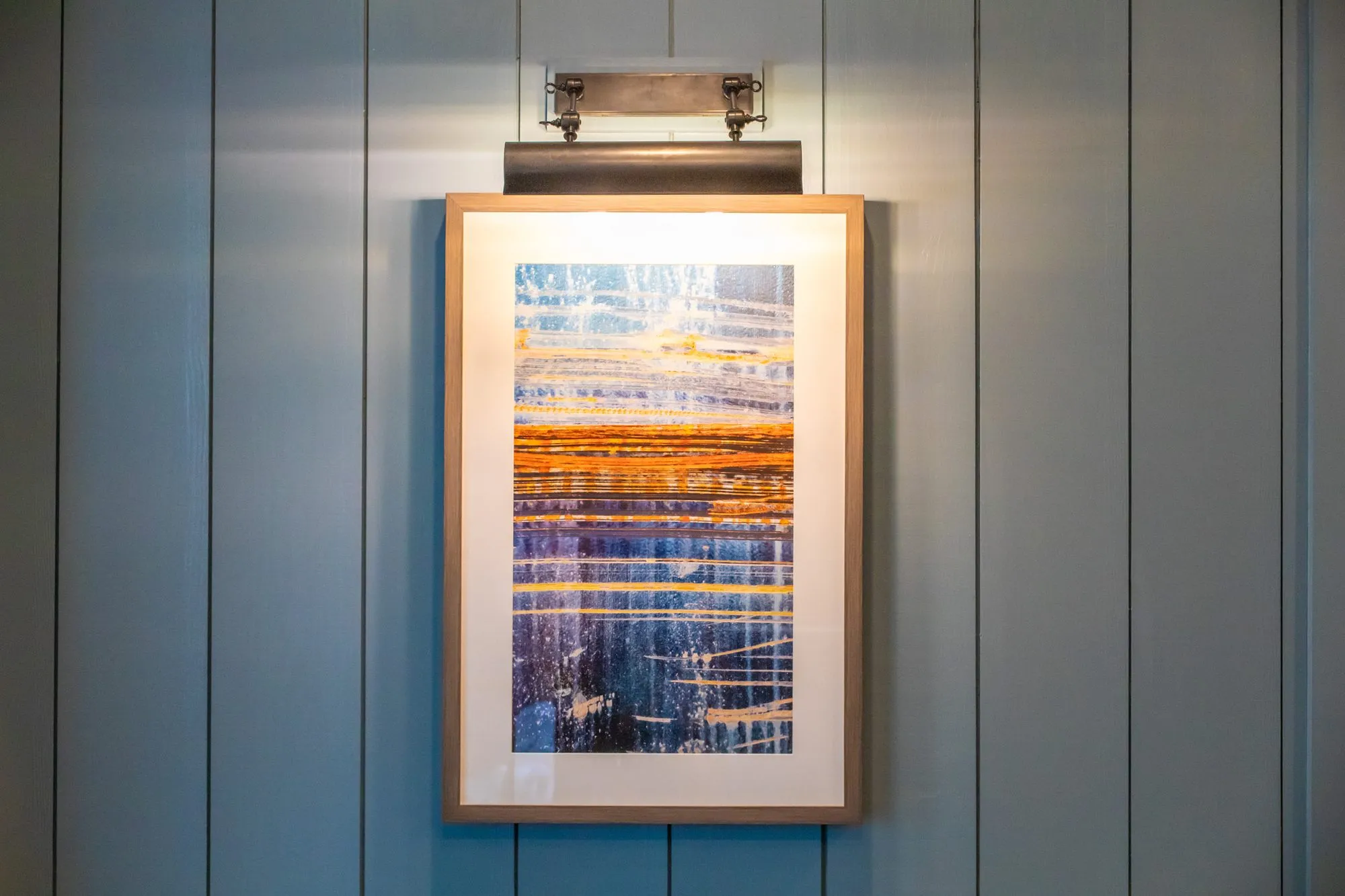 Senior living interior detail: framed abstract in blue and orange streaks with a picture light on grey blue paneling