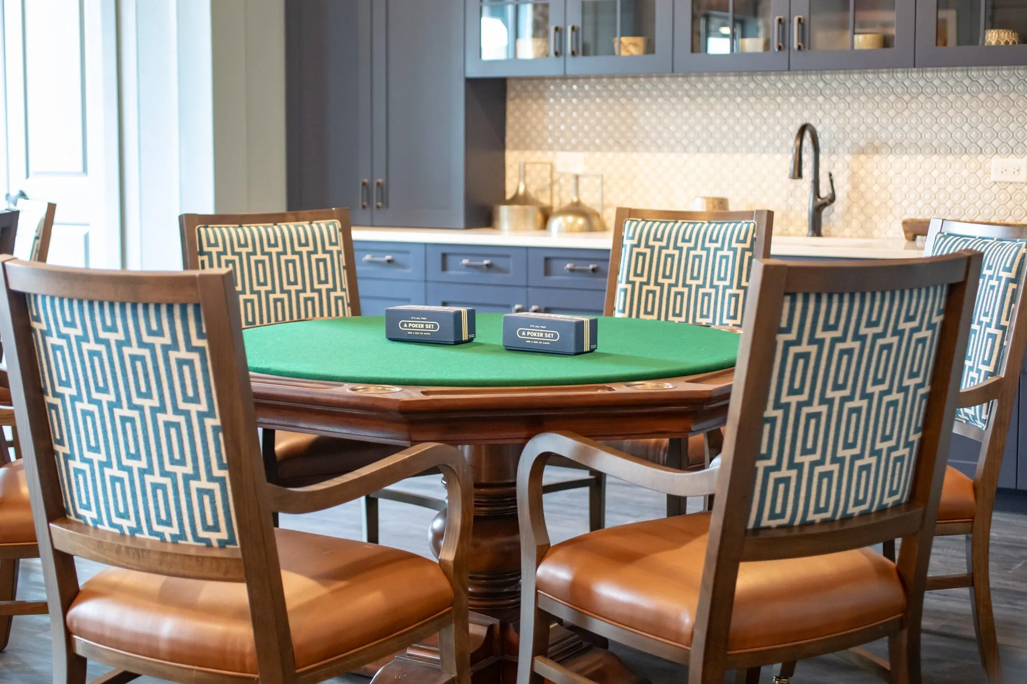 Senior living card room with a green felt card table and Greek key chairs before a grey cabinet kitchenette