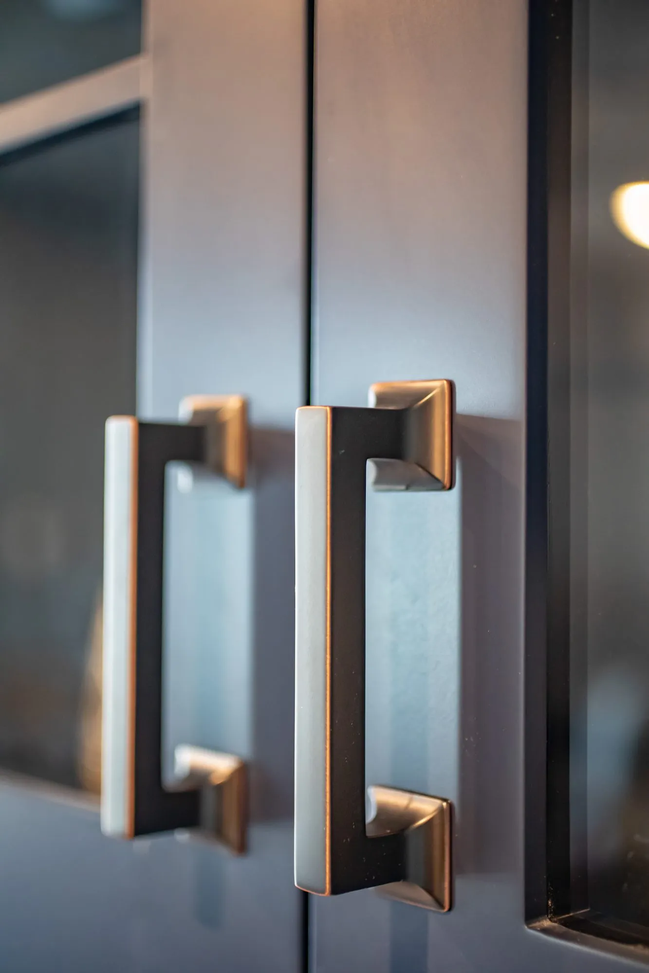 Senior living interior detail: bronze cup pulls on navy glass front cabinet doors