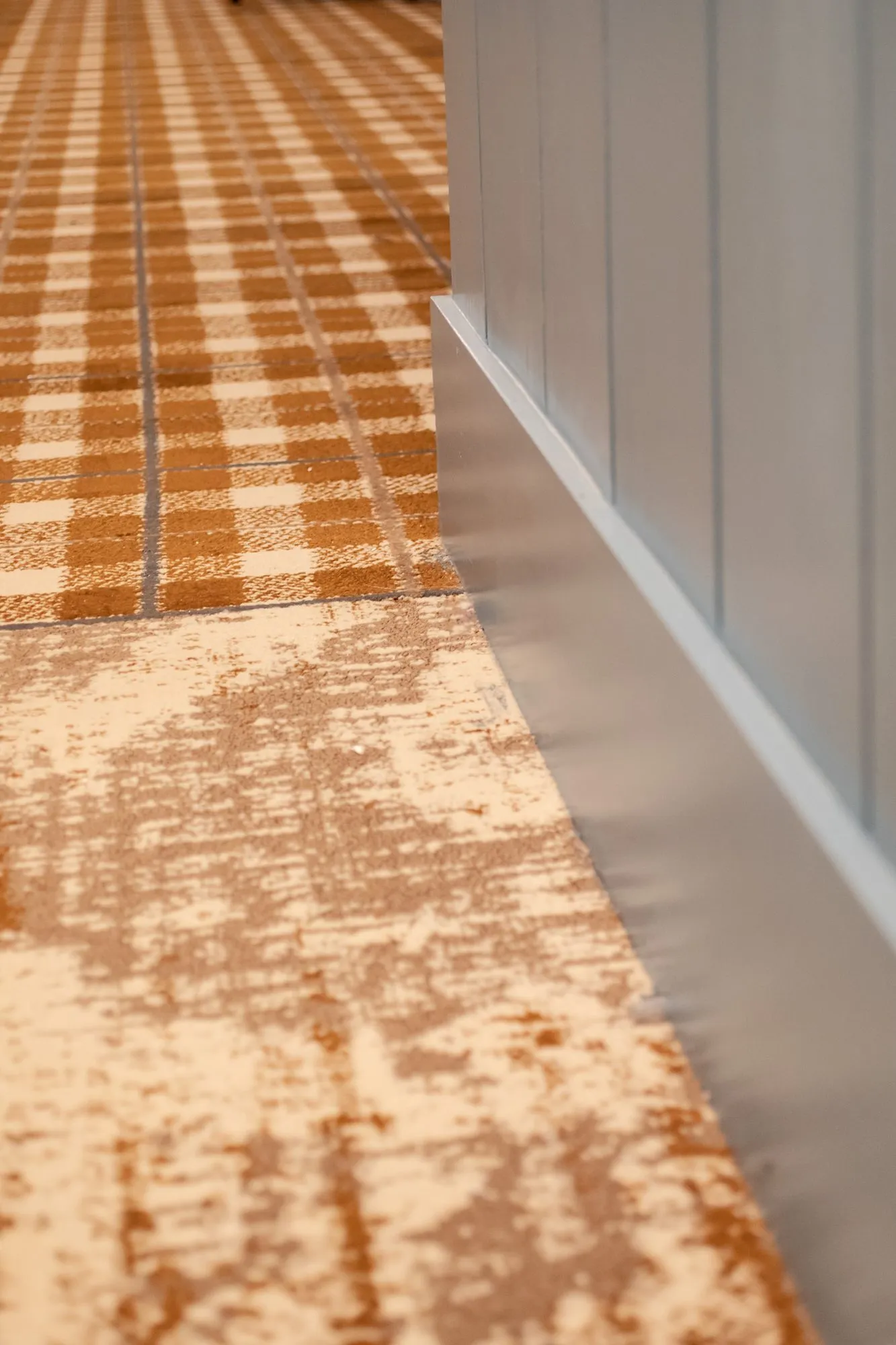 Senior living corridor floor where orange plaid carpet meets a distressed pattern runner beside blue wainscot