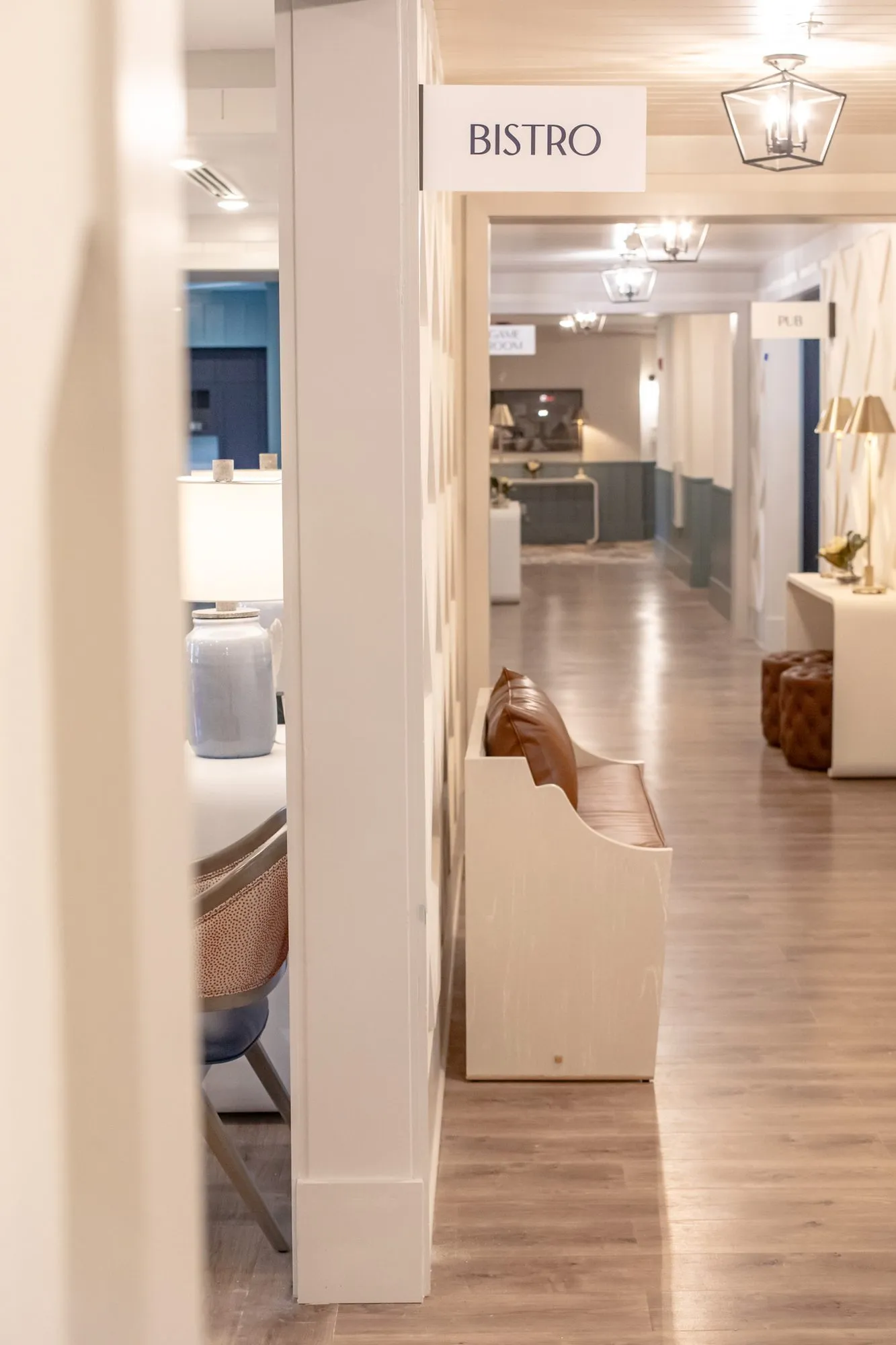 Senior living corridor with a wood bench toward a Bistro sign and lantern pendants