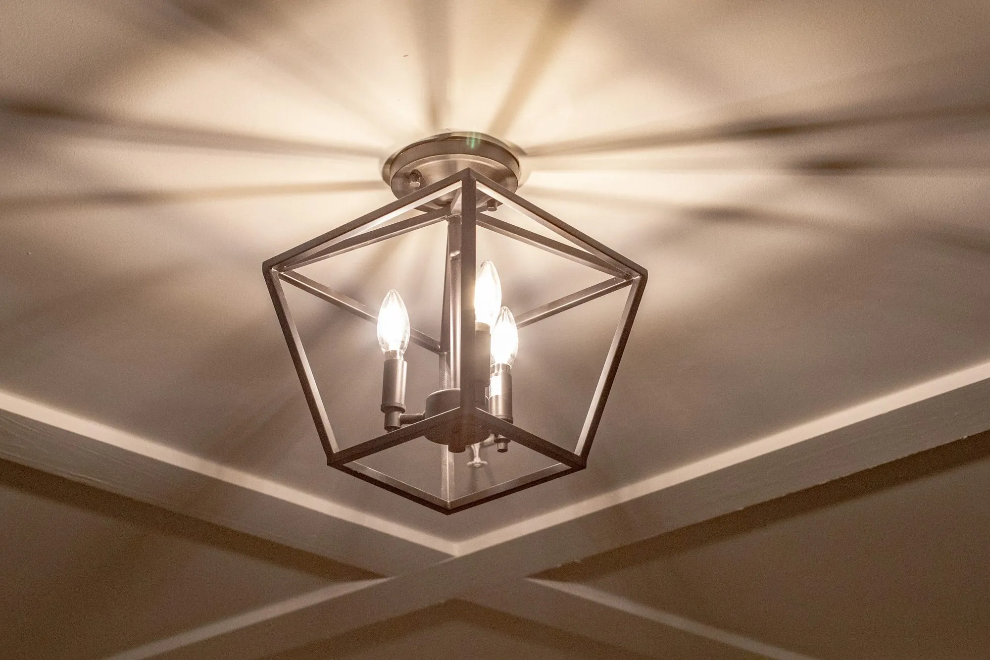 Senior living interior detail: looking up at a black lantern fixture with candle lights against a coffered ceiling