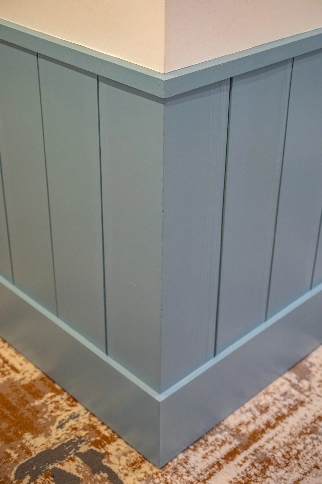 Senior living interior detail: outside corner of blue grey vertical wainscot above patterned carpet