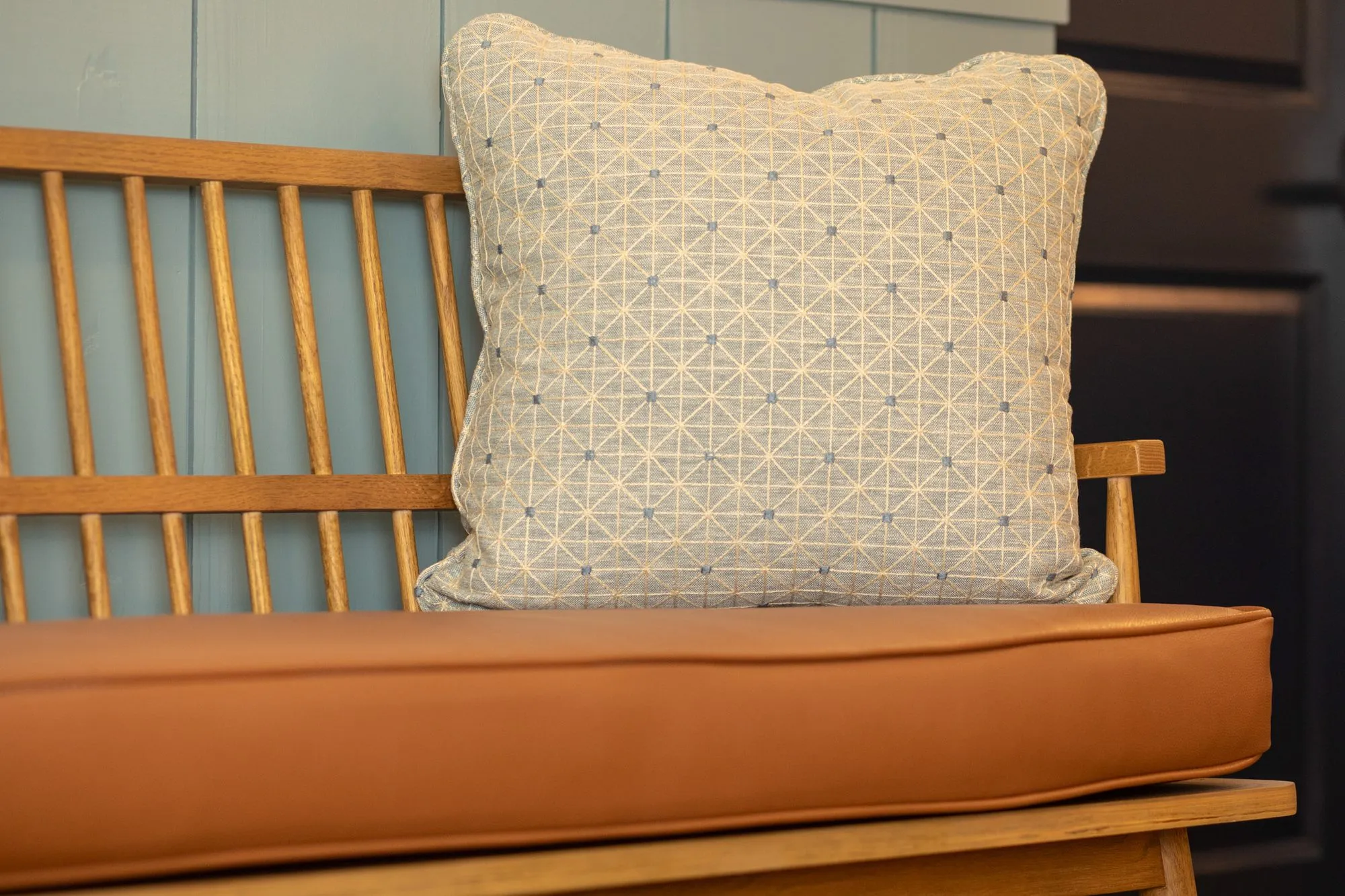 Senior living interior detail: spindle back bench with a cognac leather seat and a blue patterned pillow on blue paneling
