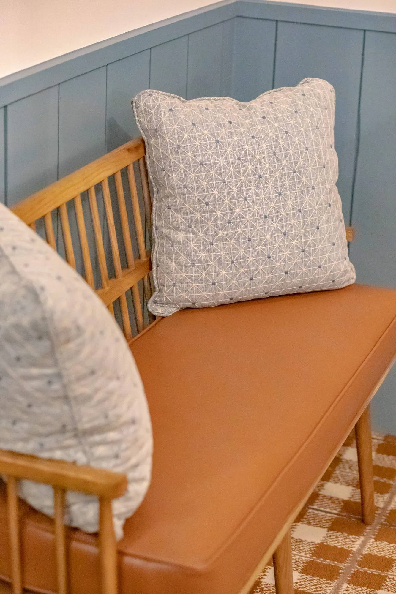 Senior living interior detail: spindle back bench with a cognac cushion and two patterned pillows on plaid carpet