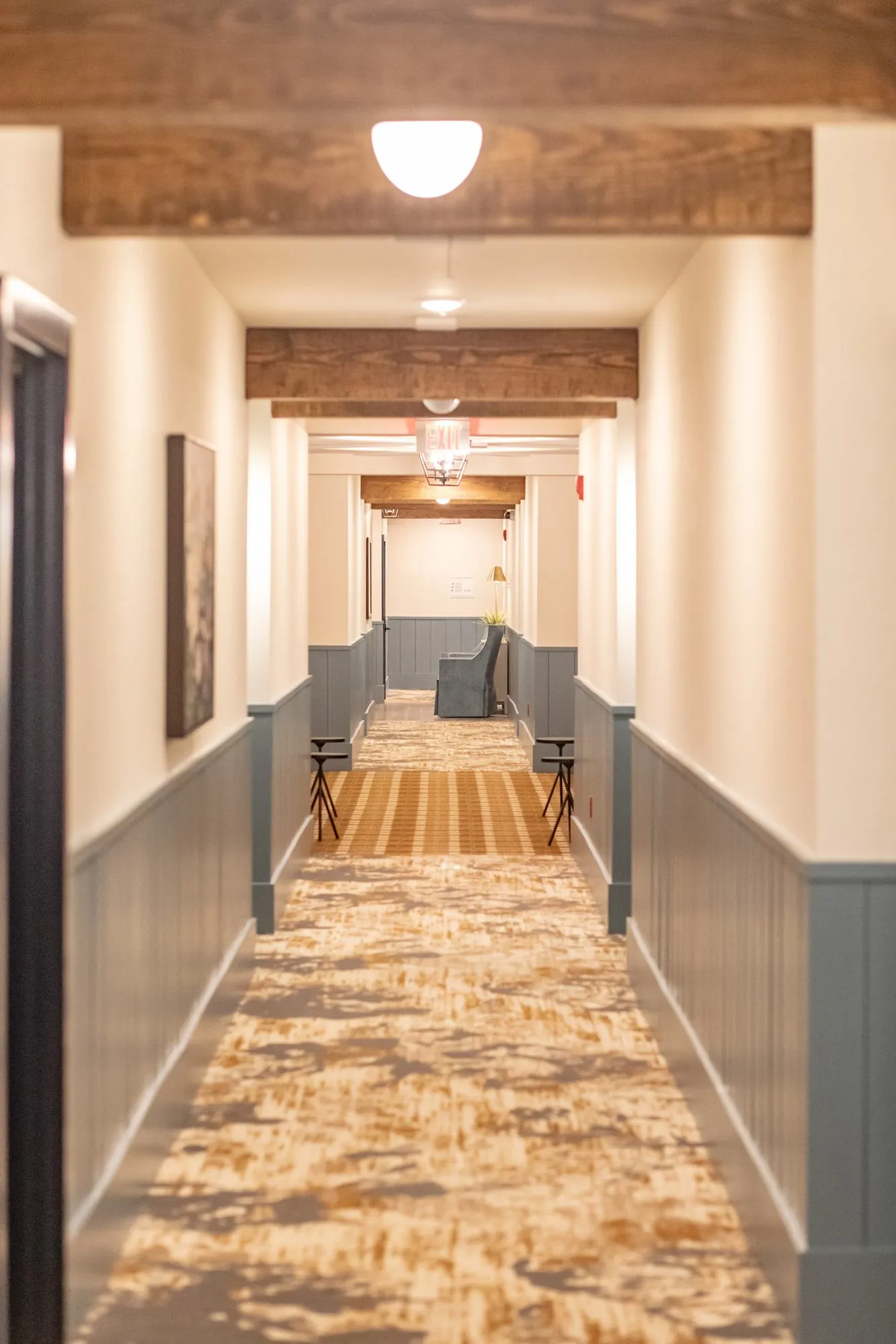 Senior living long corridor with blue wainscot, timber beams and pendant lights