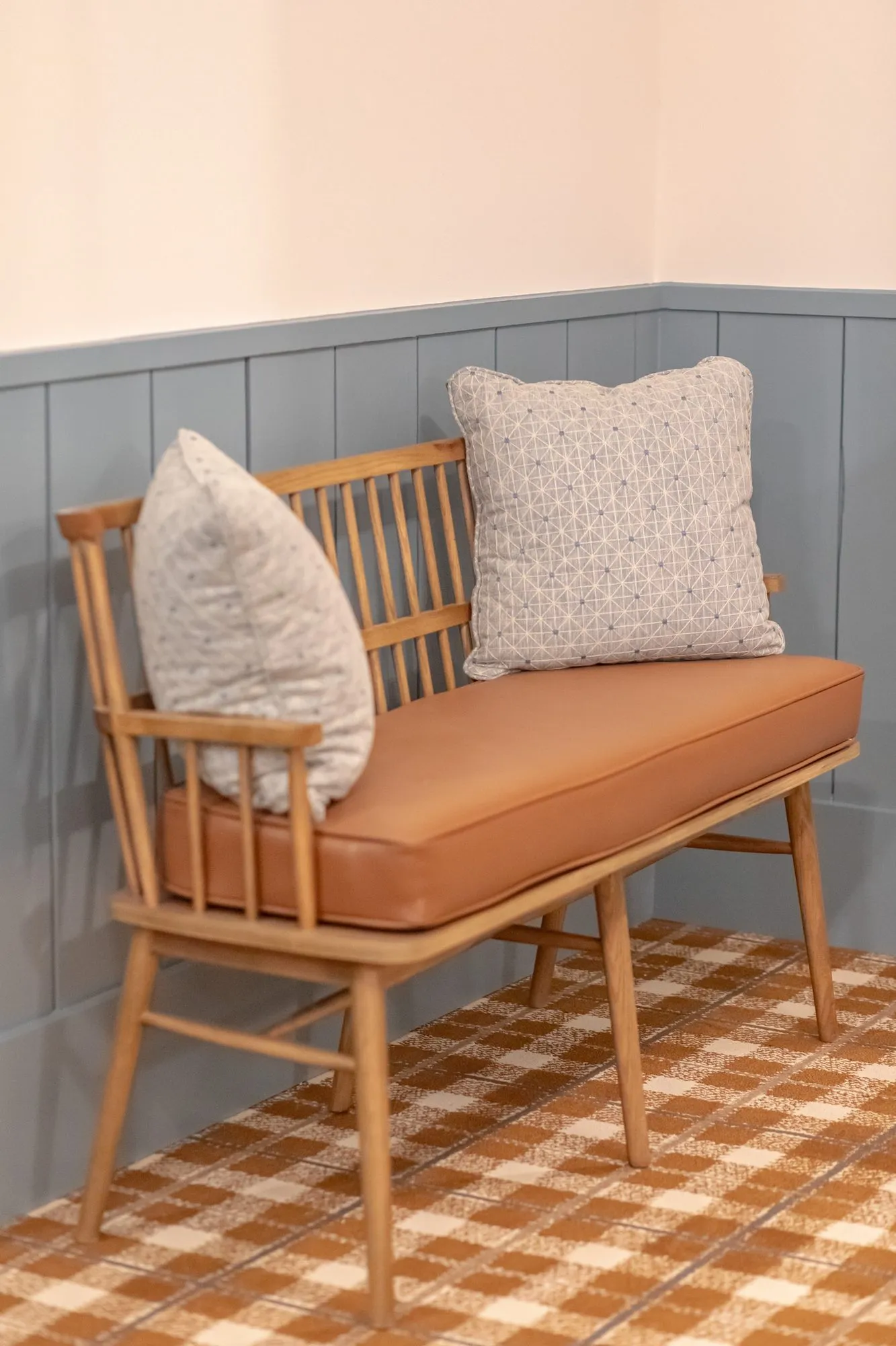 Senior living interior detail: spindle back bench with a cognac cushion and pillows against blue wainscot