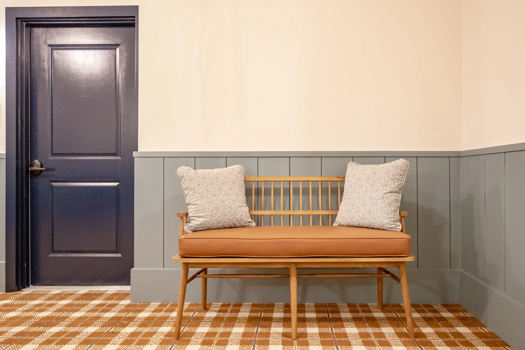 Senior living interior detail: spindle back bench with a cognac cushion and pillows beside a navy door, blue wainscot