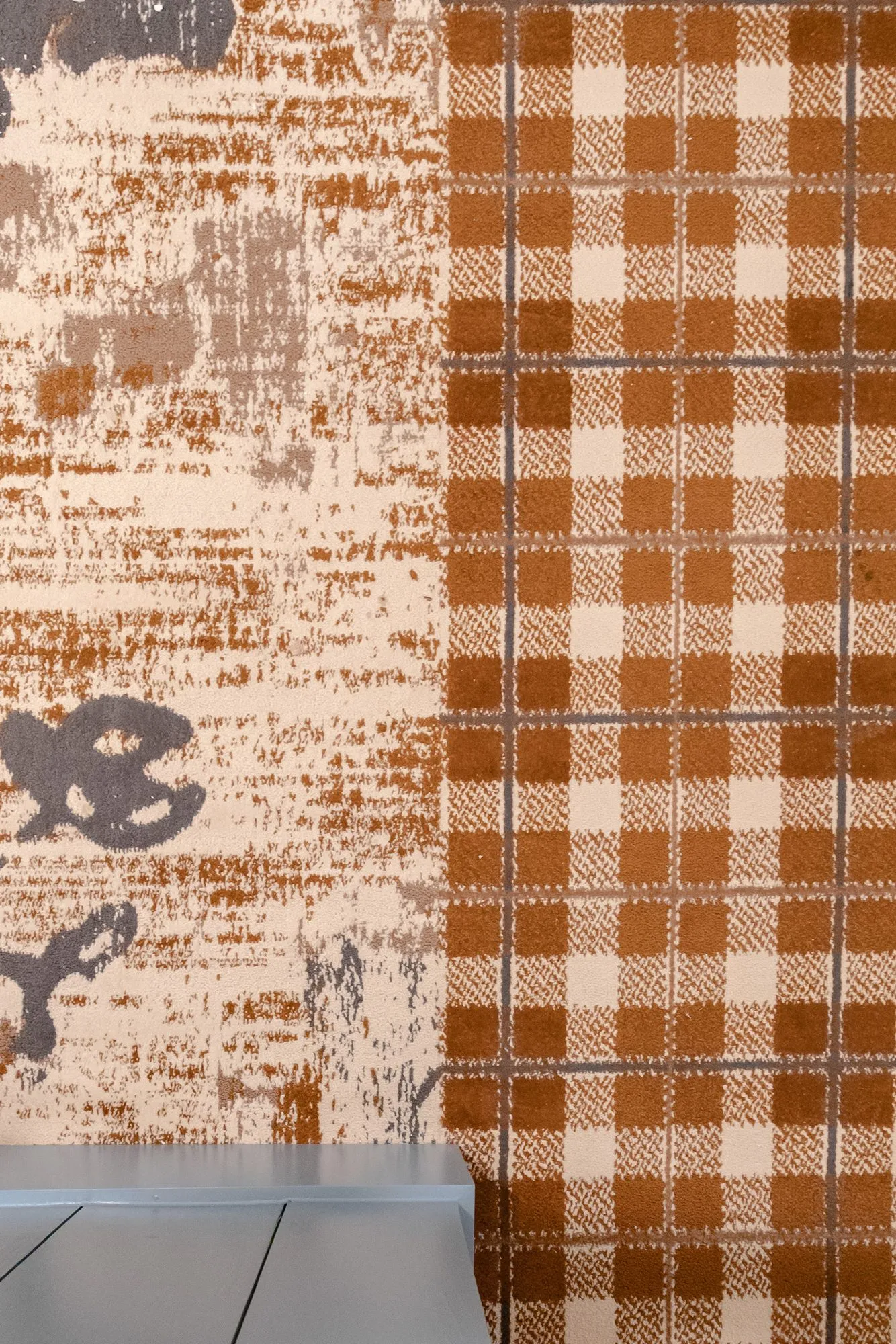 Senior living interior detail: distressed pattern carpet meeting orange plaid carpet at a blue baseboard