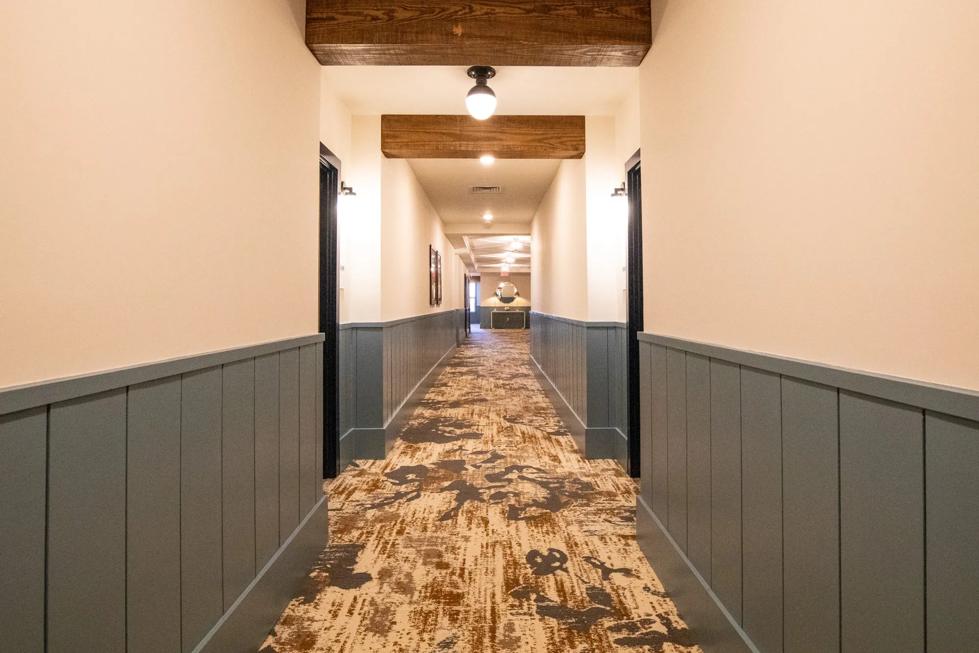 Senior living corridor with blue grey wainscot, a patterned runner and timber beams leading into the distance