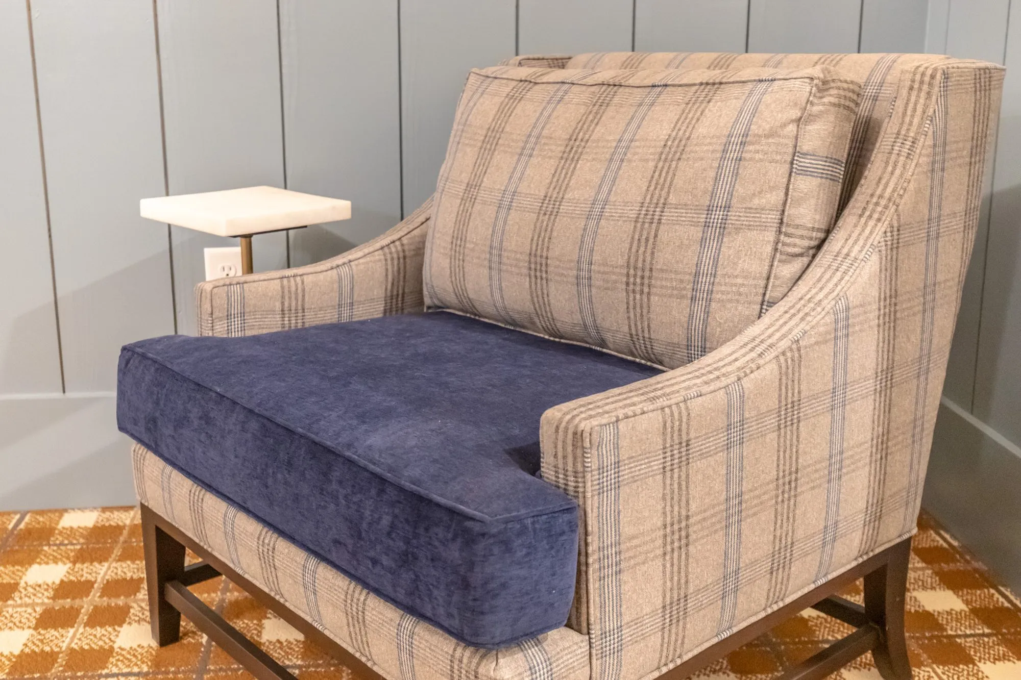 Senior living interior detail: plaid armchair with a navy velvet seat beside a white drink table on plaid carpet