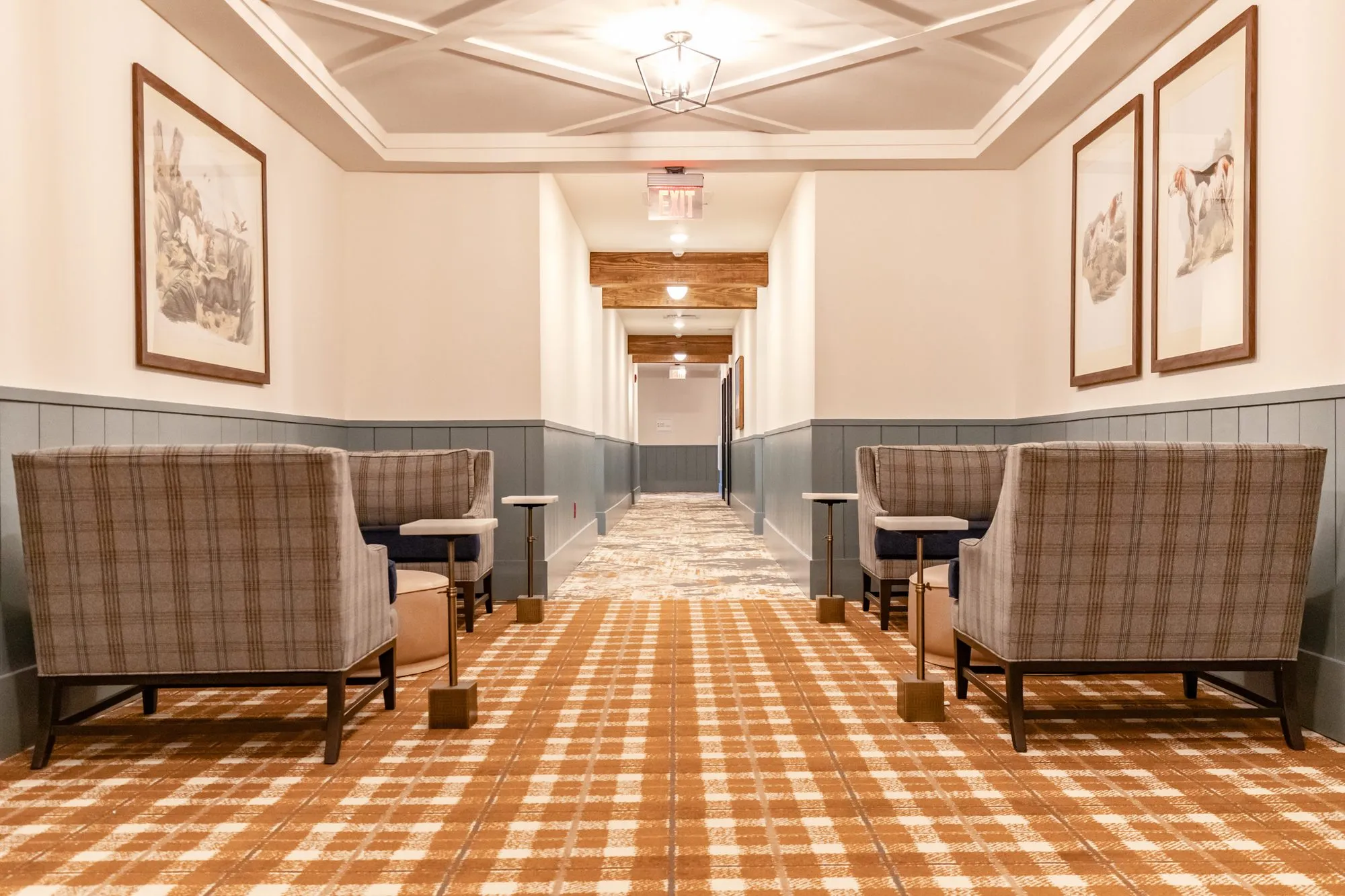 Senior living corridor sitting area with plaid armchairs and drink tables facing each other, framed dog prints