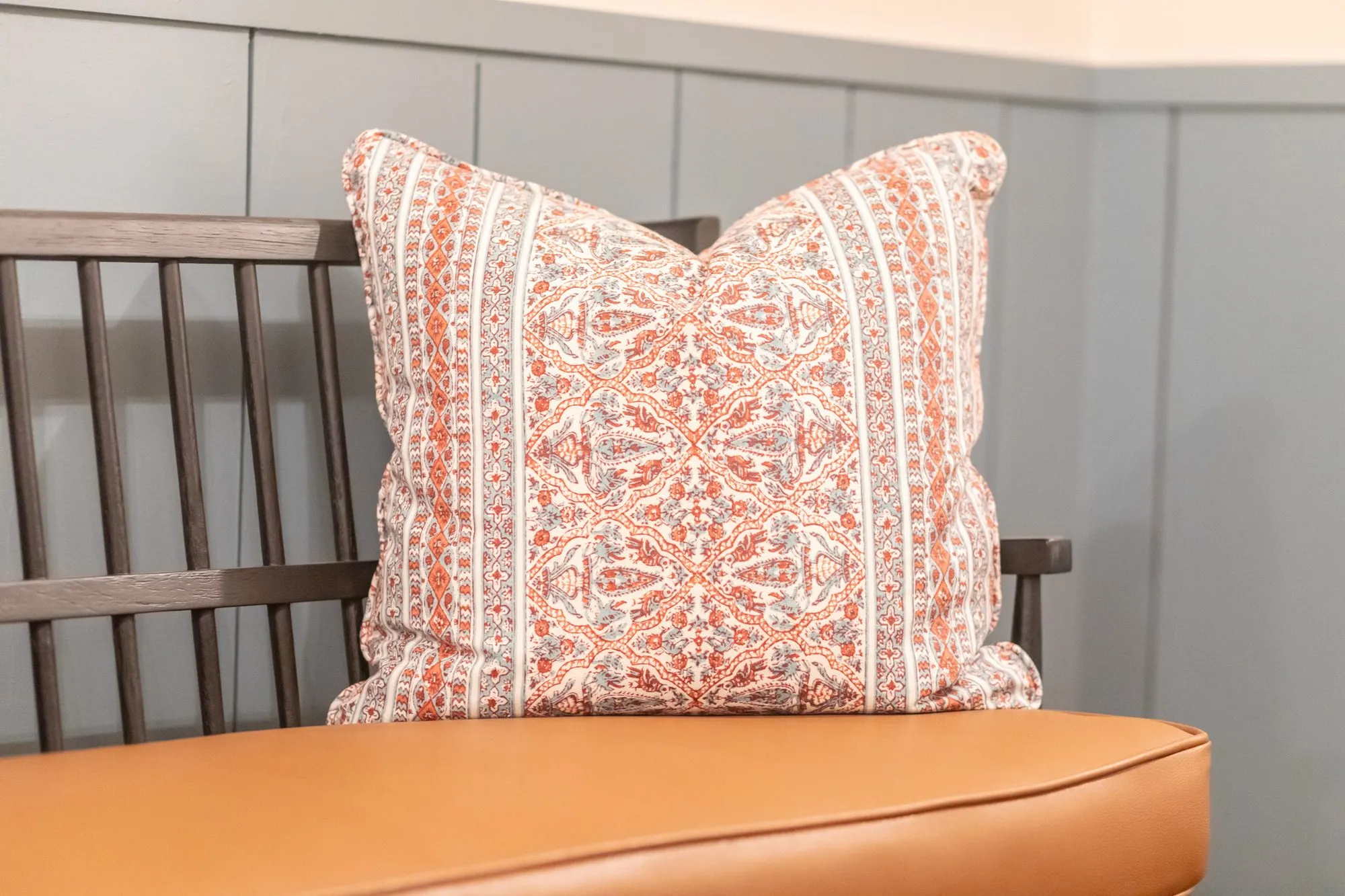 Senior living interior detail: coral and blue paisley stripe pillow on a cognac bench seat against blue paneling