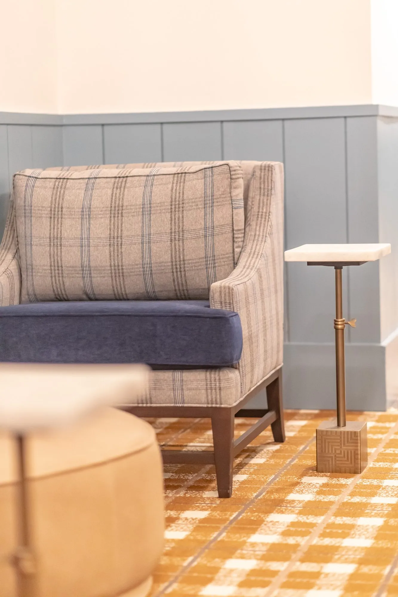 Senior living interior detail: plaid armchair with a navy seat and a slim stone topped drink table on plaid carpet