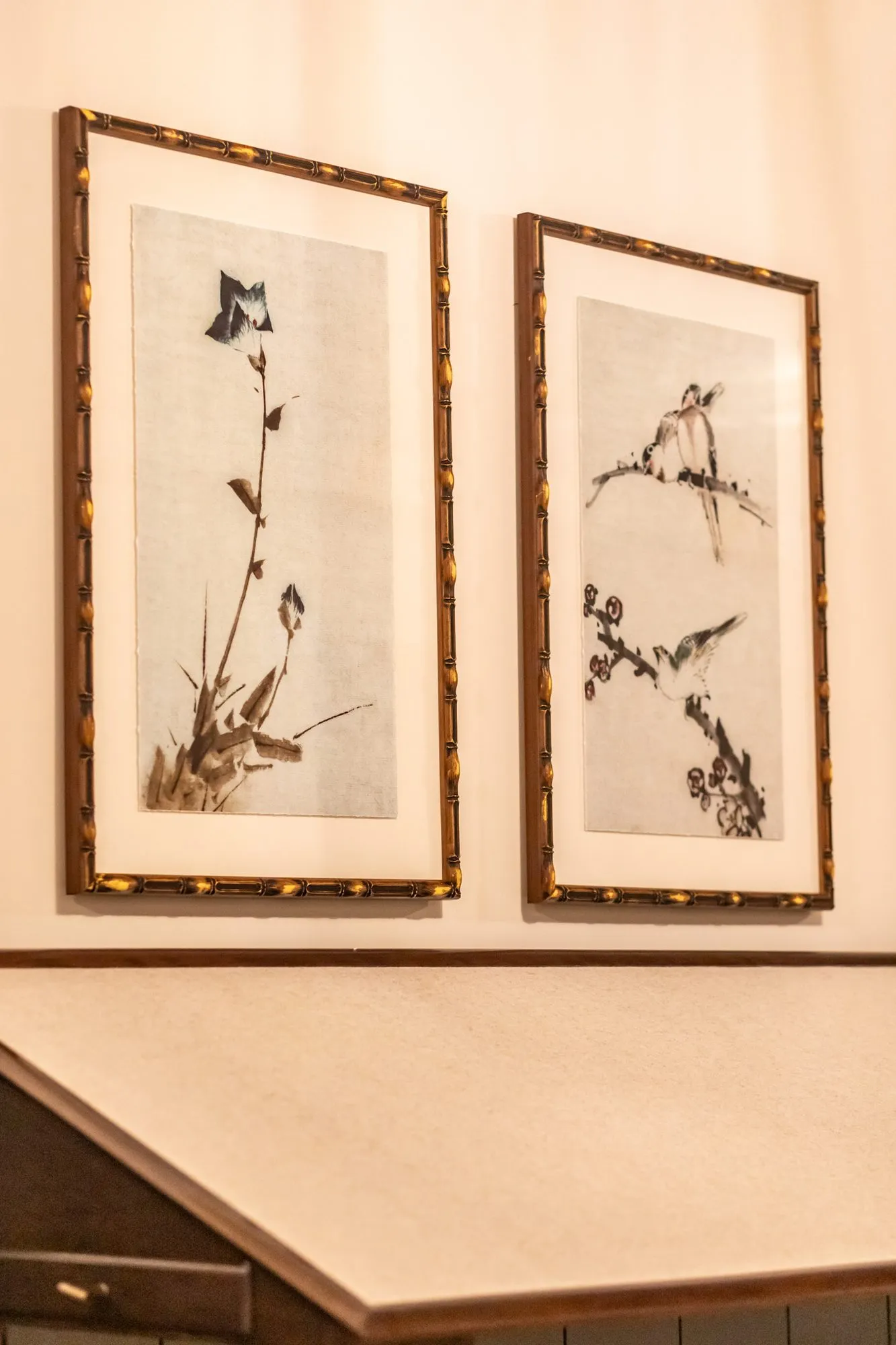 Senior living interior detail: two bamboo framed bird and blossom prints above a desk, seen at an angle