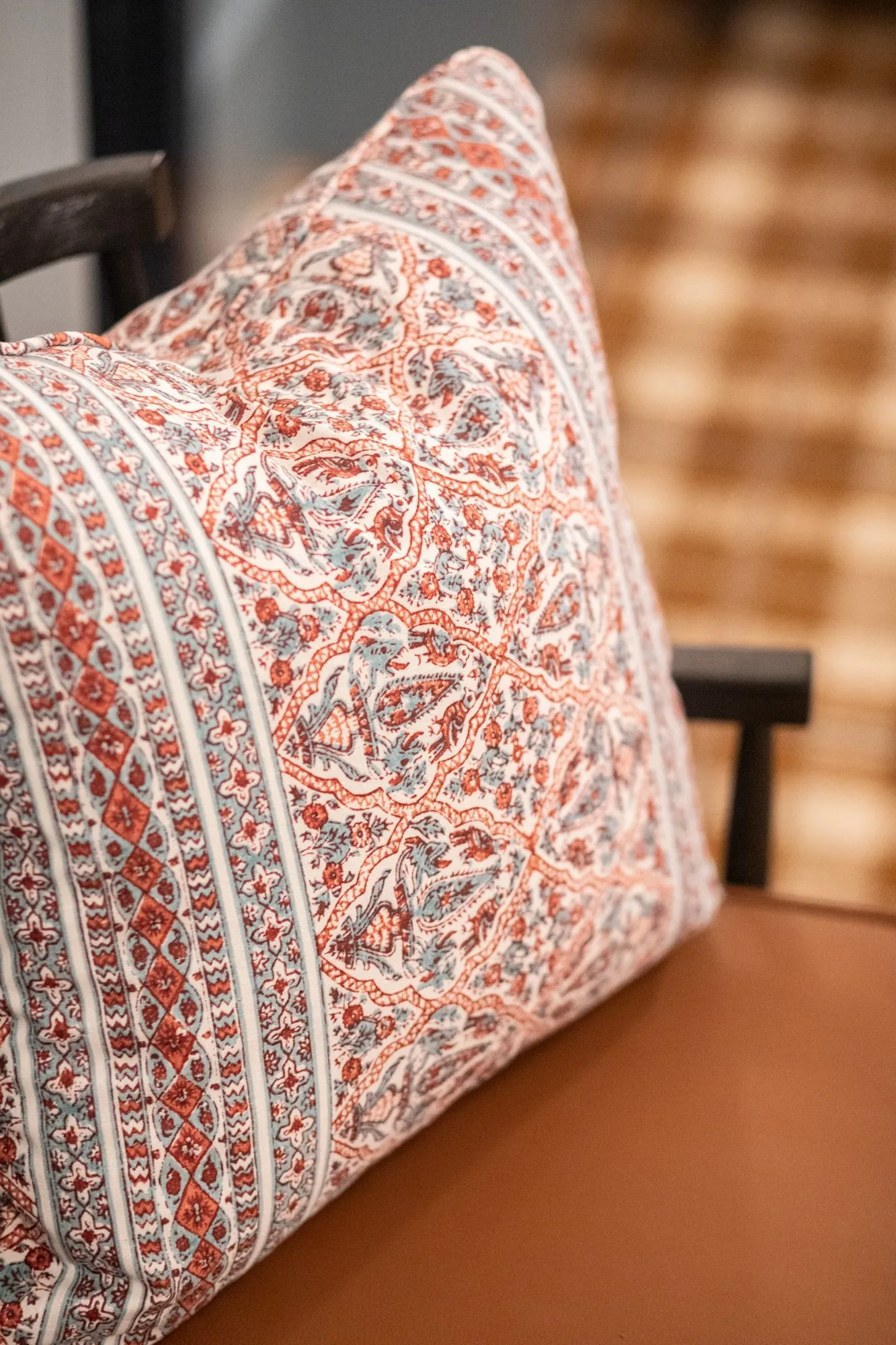 Senior living interior detail: coral paisley stripe pillow on a cognac seat beside plaid fabric