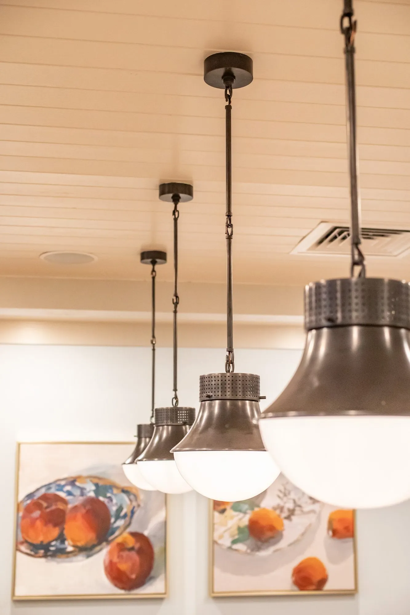 Senior living interior detail: bronze and opal glass pendants in a row before framed paintings of peaches