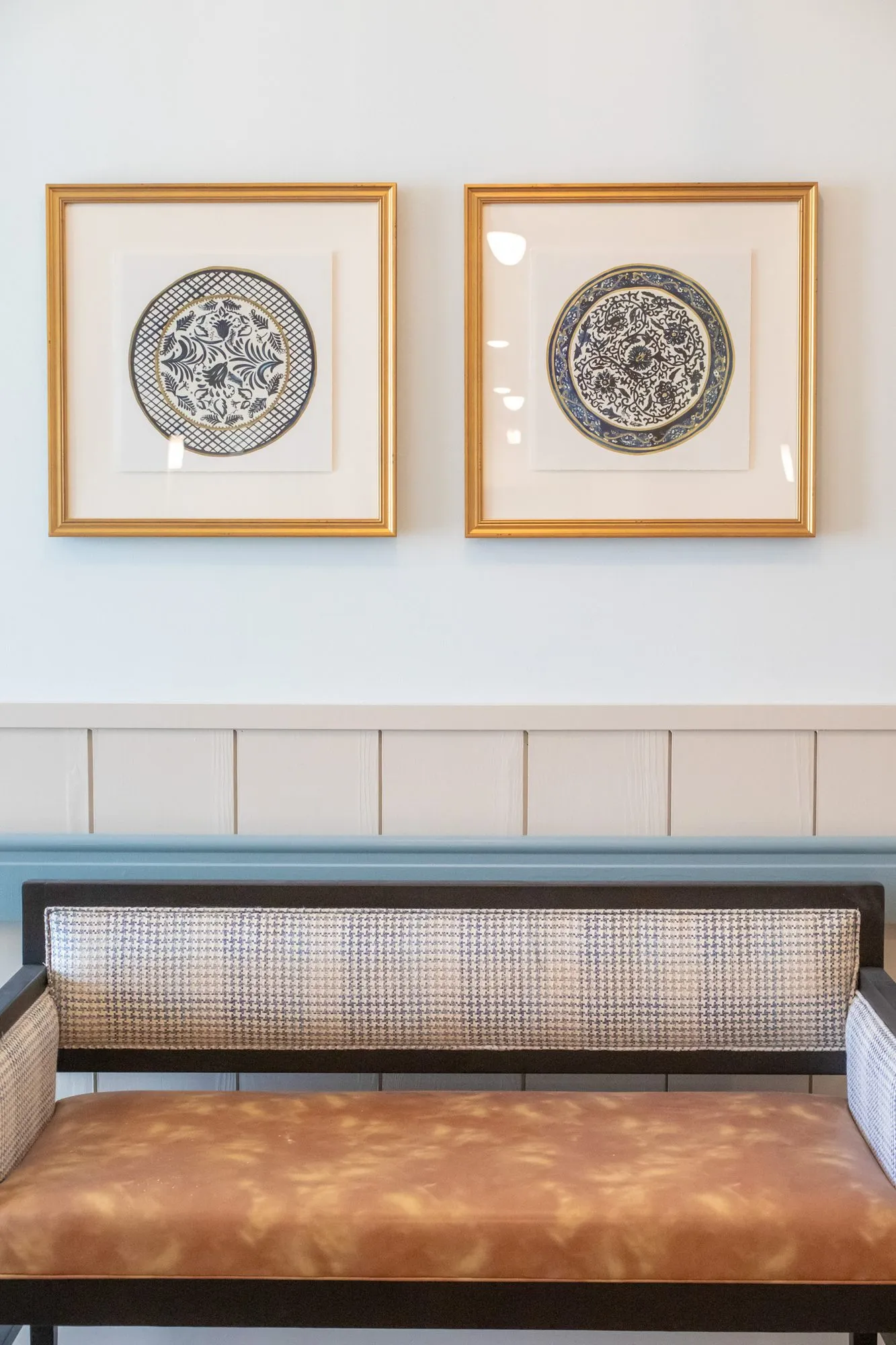 Senior living interior detail: cane back bench with a cognac seat below two framed blue and white plate prints