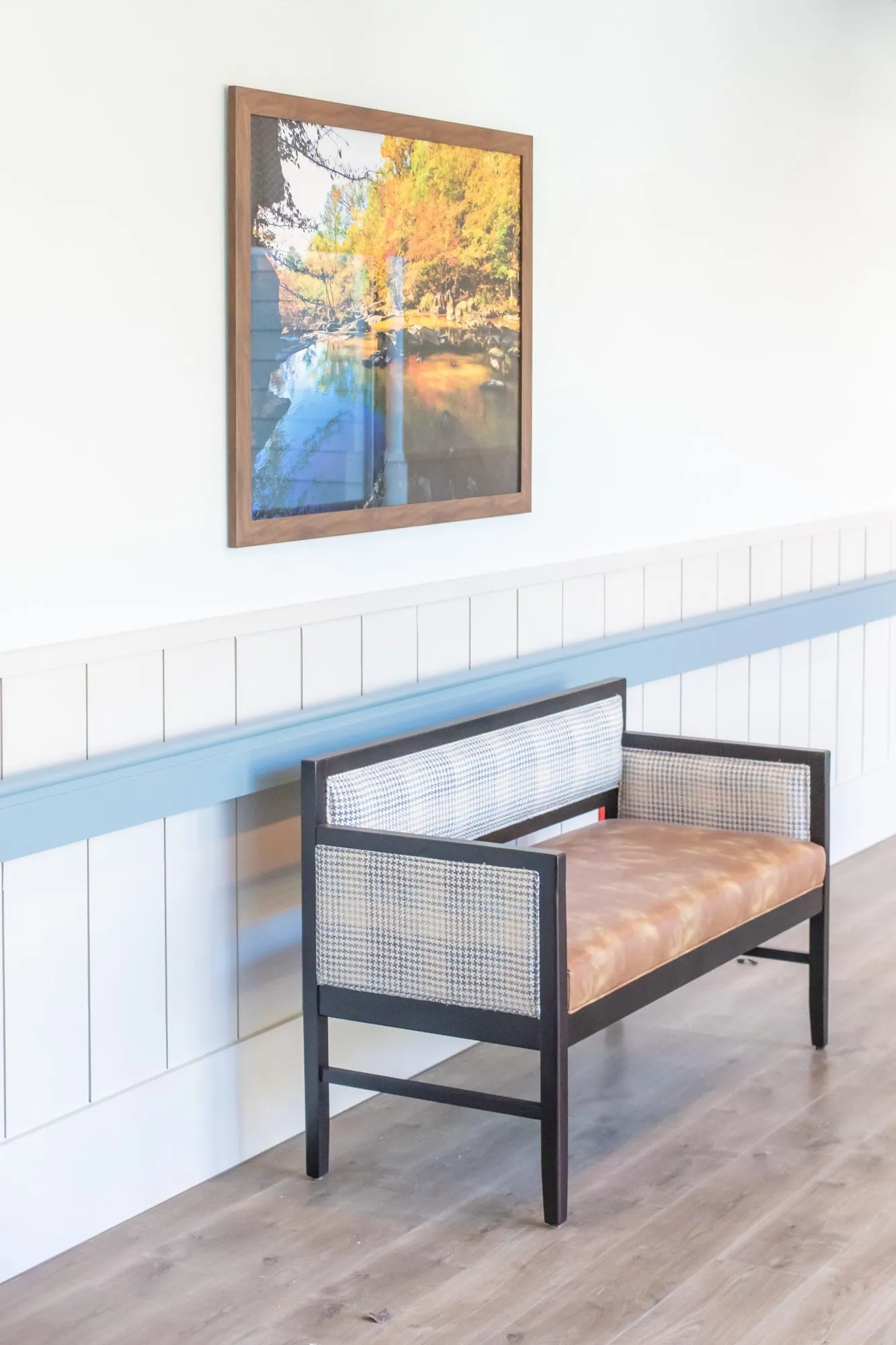 Senior living corridor with a cane back bench and cognac seat below an autumn landscape photograph