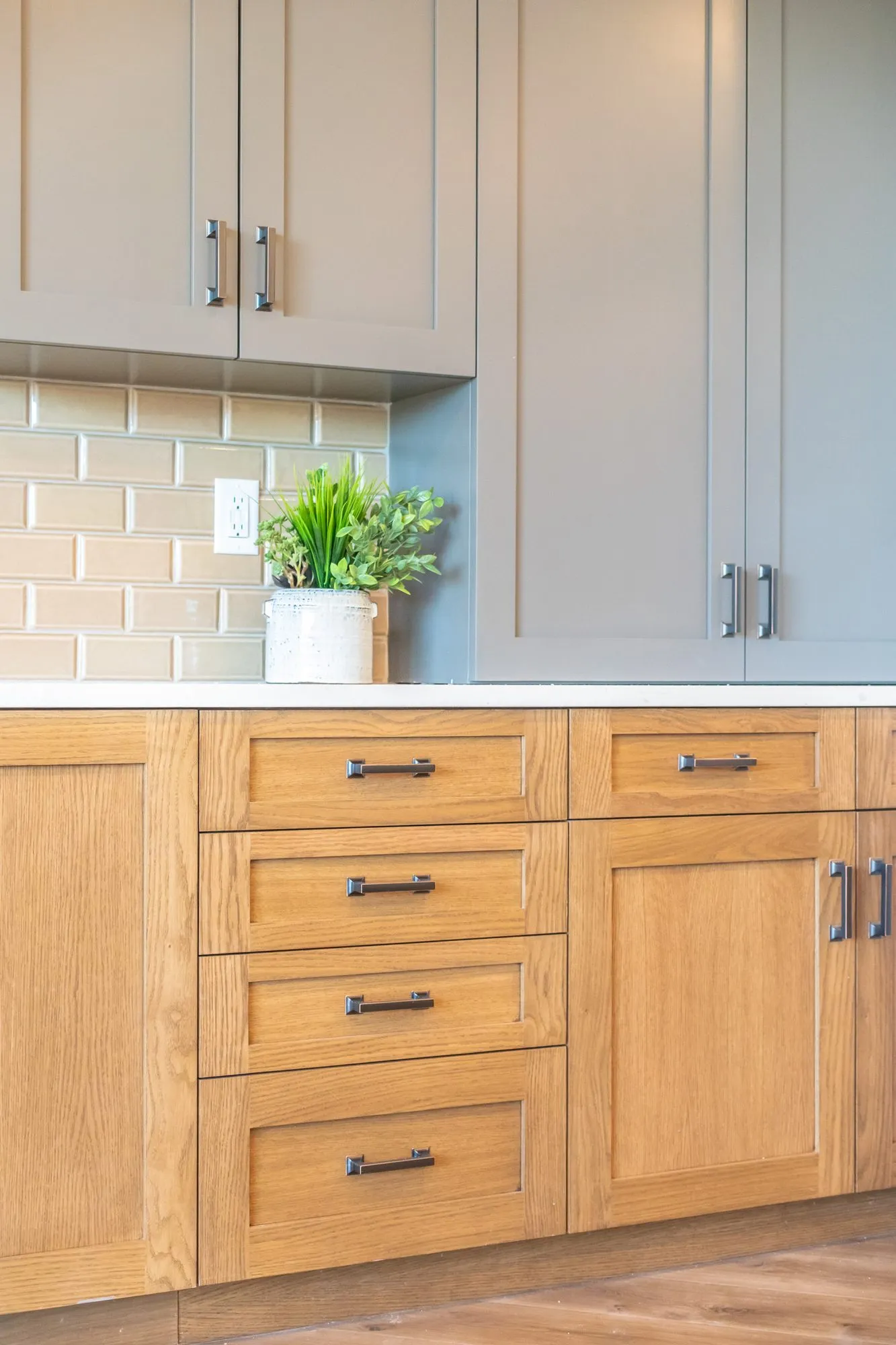 Senior living interior detail: oak lower cabinets with drawers and grey uppers around tan subway tile and a plant