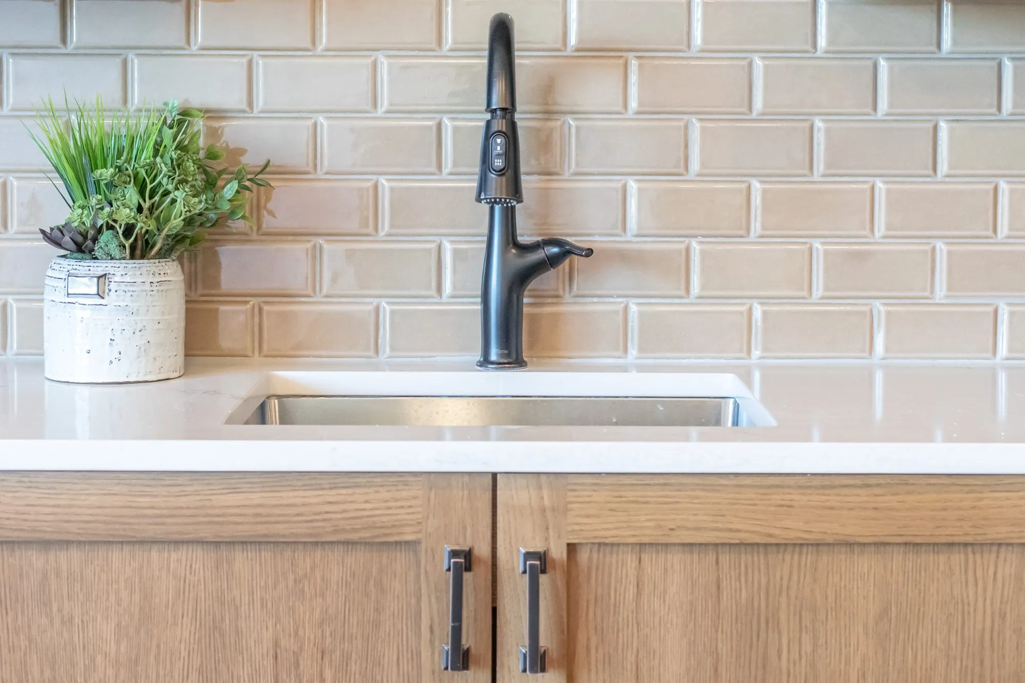 Senior living interior detail: matte black faucet over a stainless sink, oak cabinets and tan subway tile