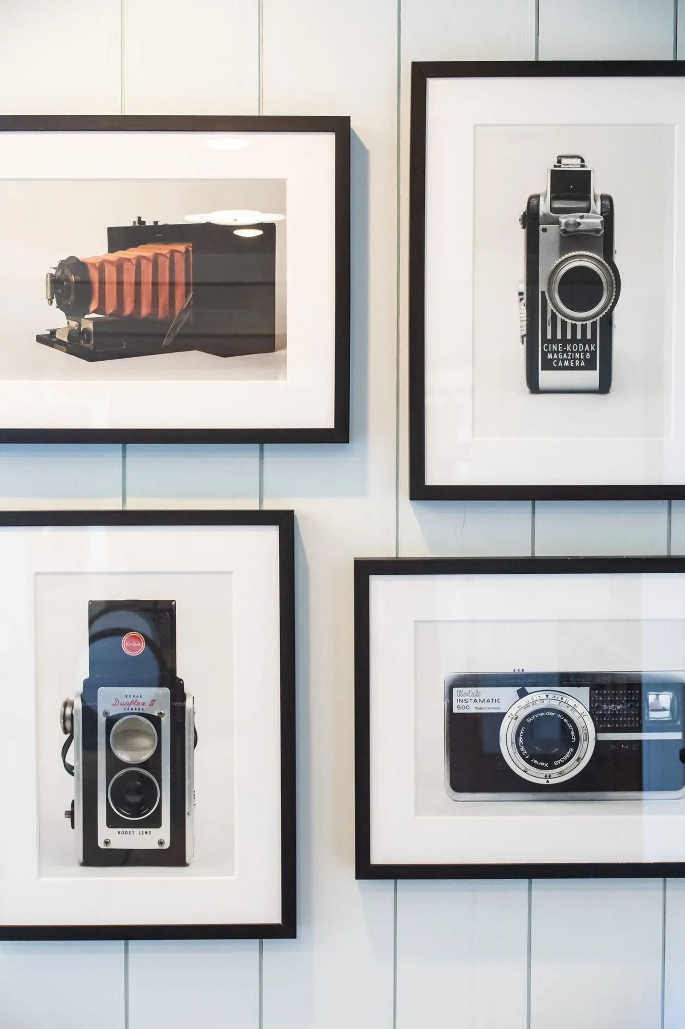 Senior living interior detail: four framed photographs of vintage cameras on white shiplap