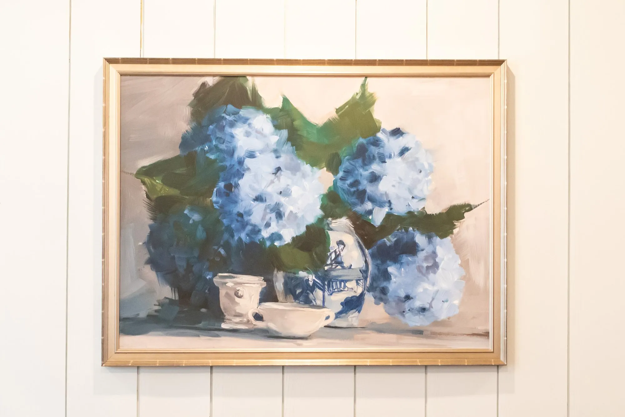 Senior living interior detail: still life of blue hydrangeas and a teapot in a gilt frame on white shiplap