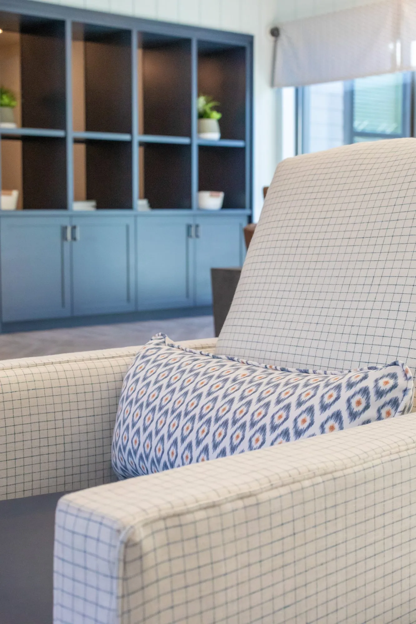 Senior living interior detail: windowpane check armchair with an ikat pillow before navy built-in shelves