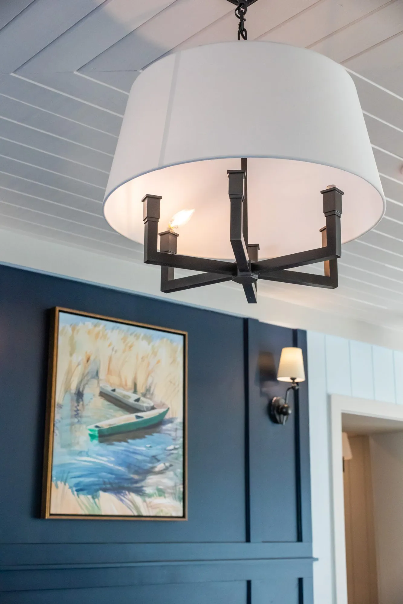 Senior living interior detail: white drum shade chandelier with black arms before a navy wall with a boat painting
