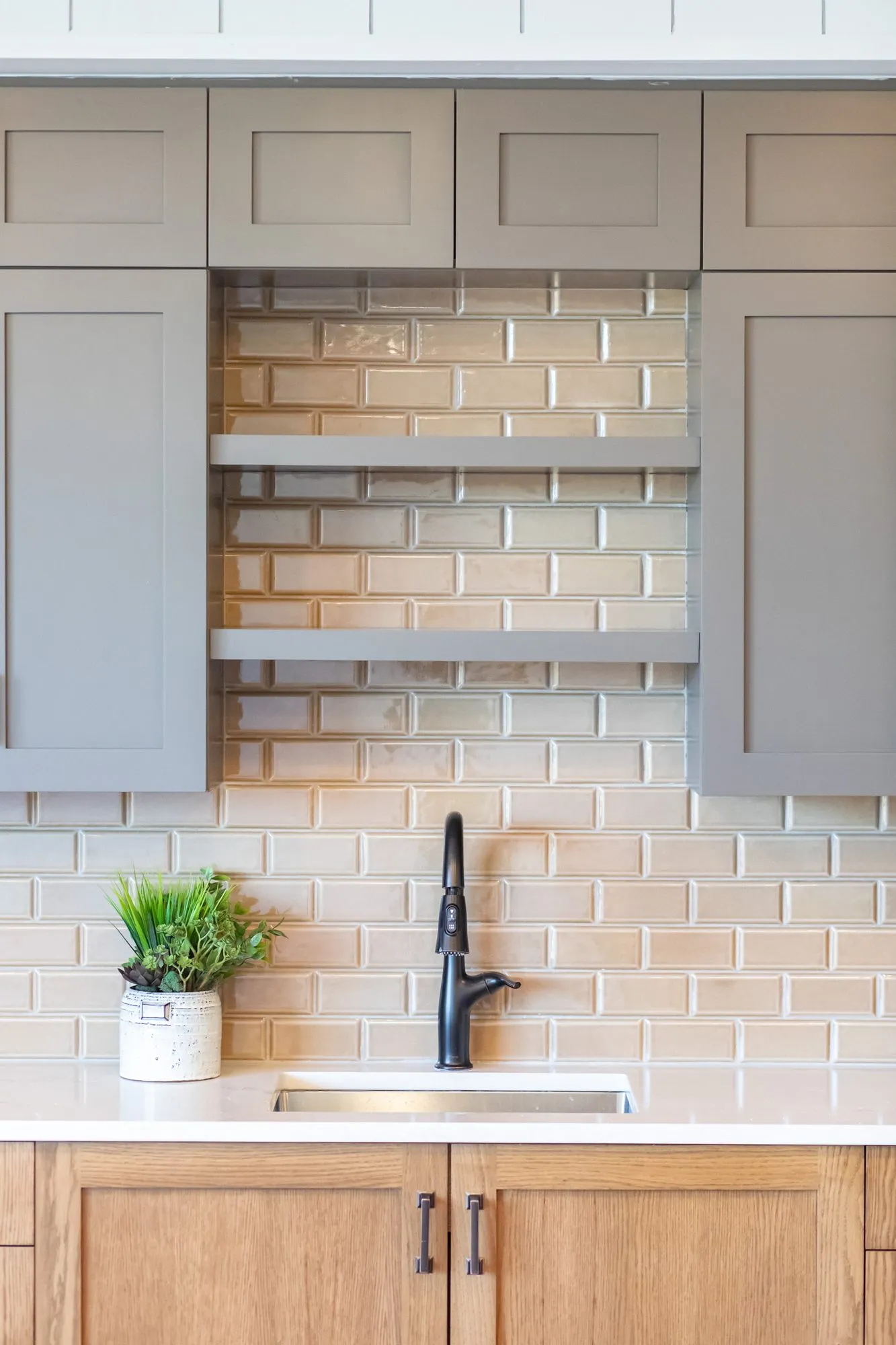 Senior living kitchenette with open shelves between grey cabinets over tan subway tile