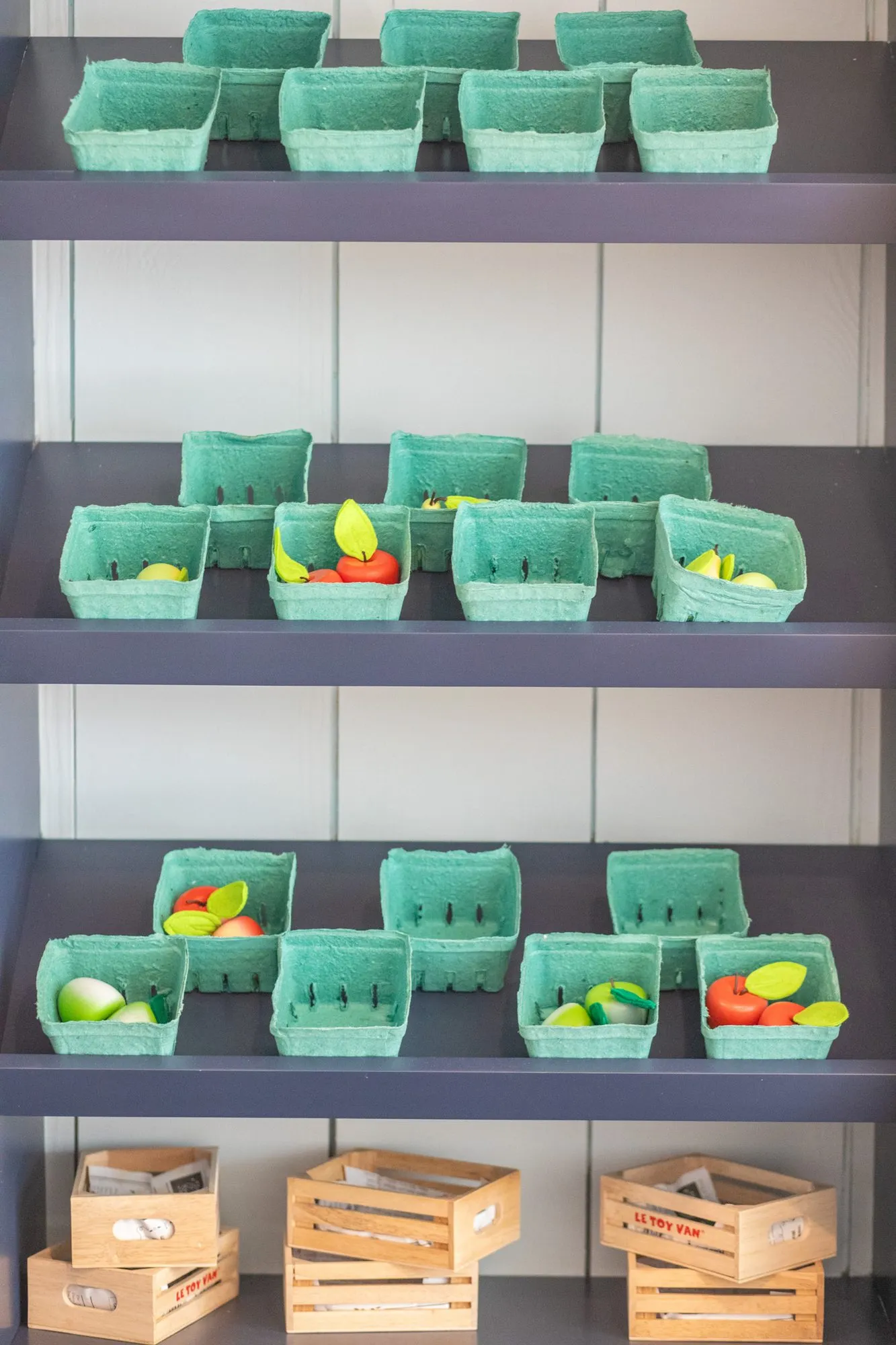 Senior living market shelving with rows of green berry baskets holding play fruit above wooden crates
