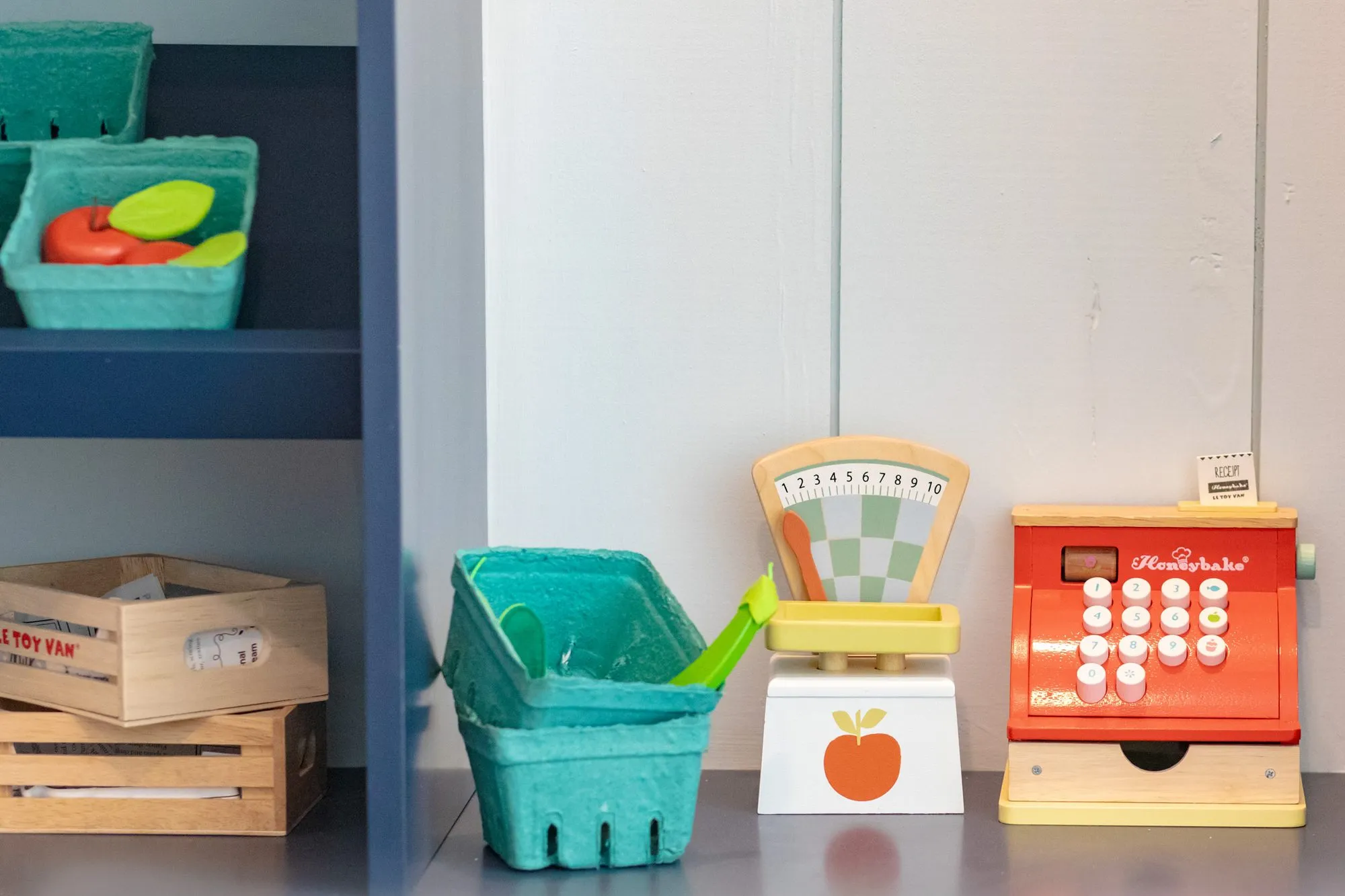 Senior living interior detail: toy cash register and scale beside green berry baskets and wooden crates on a counter
