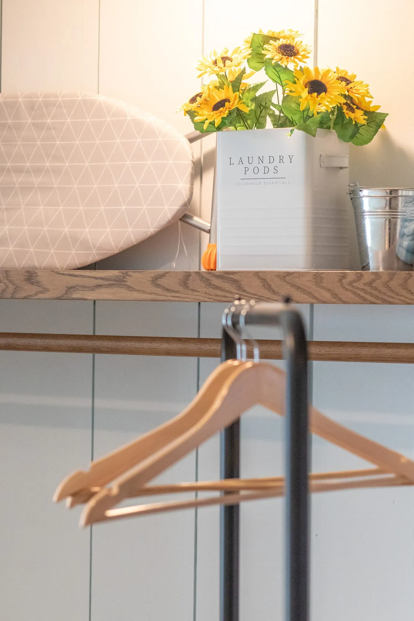 Senior living laundry vignette with an ironing board, a canister of sunflowers and wooden hangers on a rail